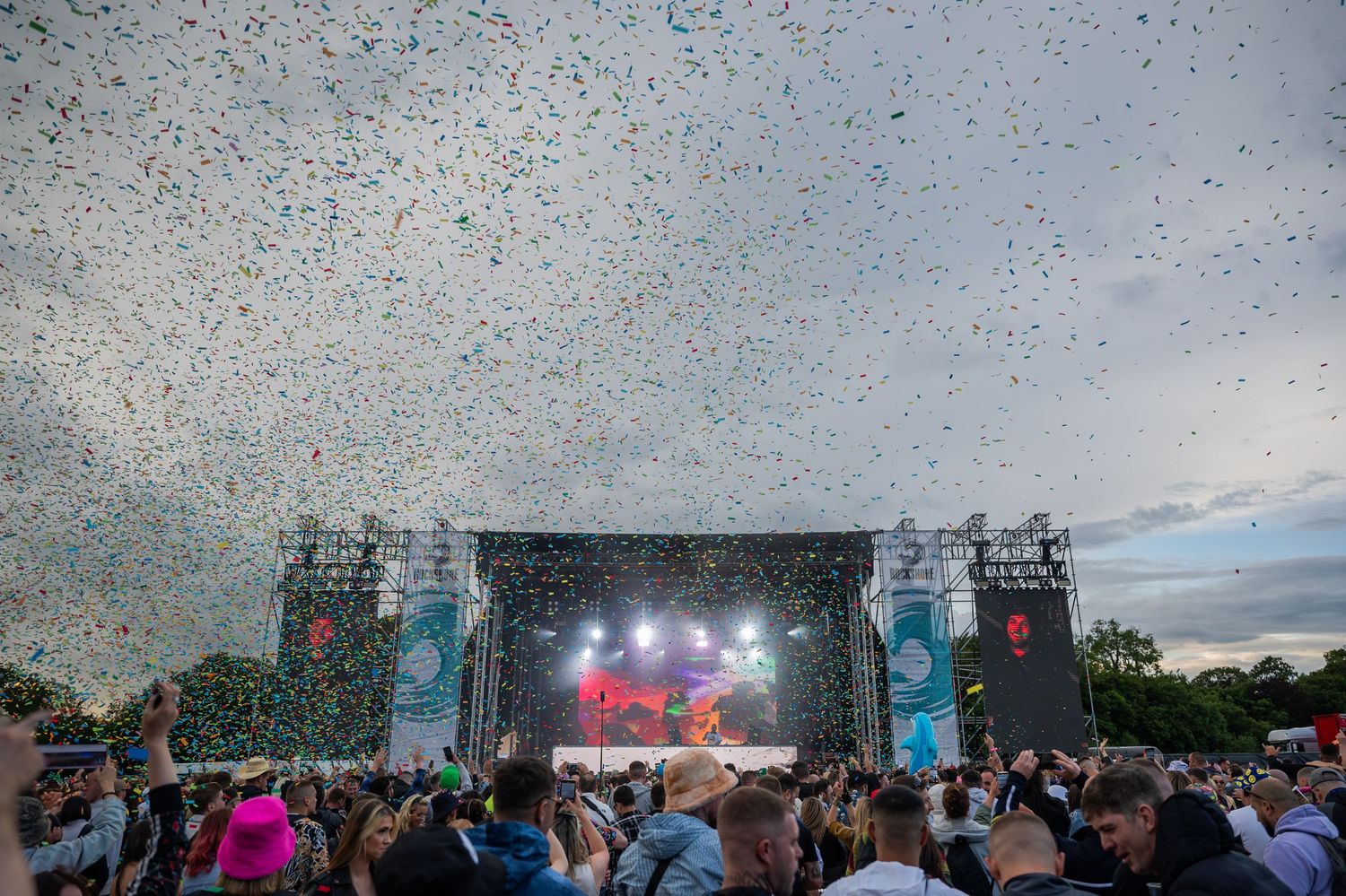 Colorful confetti fills the sky above a packed outdoor music festival stage.