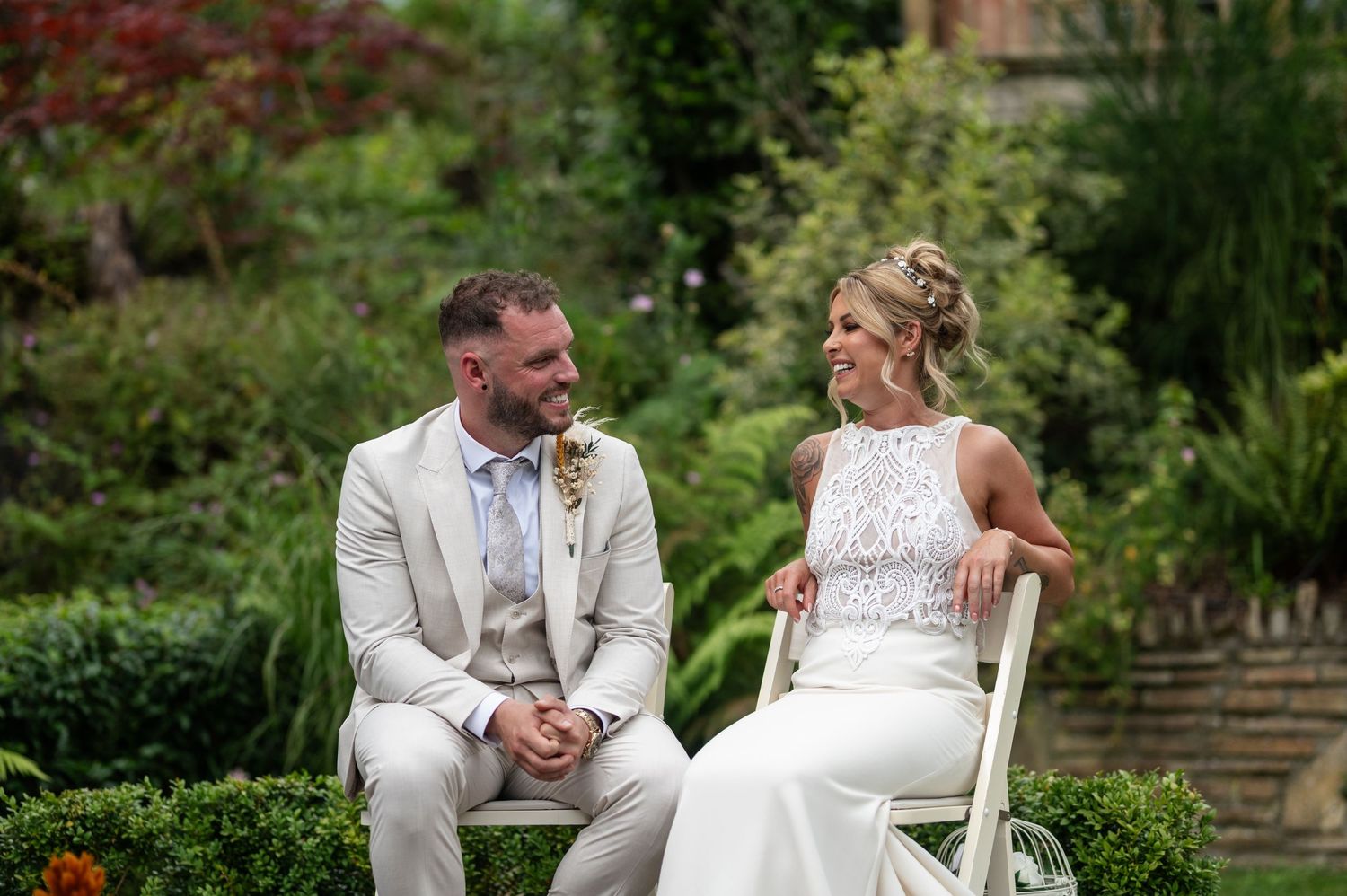 Bride and groom sharing a loving glance while seated at outdoor garden wedding.