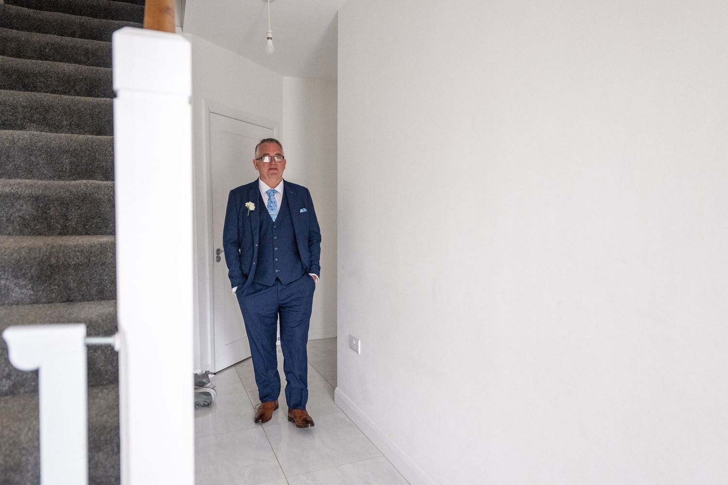 A well-dressed man in a navy blue suit stands confidently in a modern hallway near a staircase.
