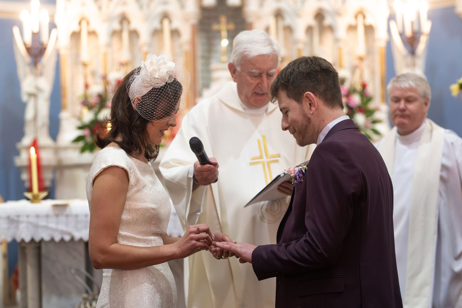 Couple exchanging rings during a church wedding ceremony with a priest officiating at the altar.