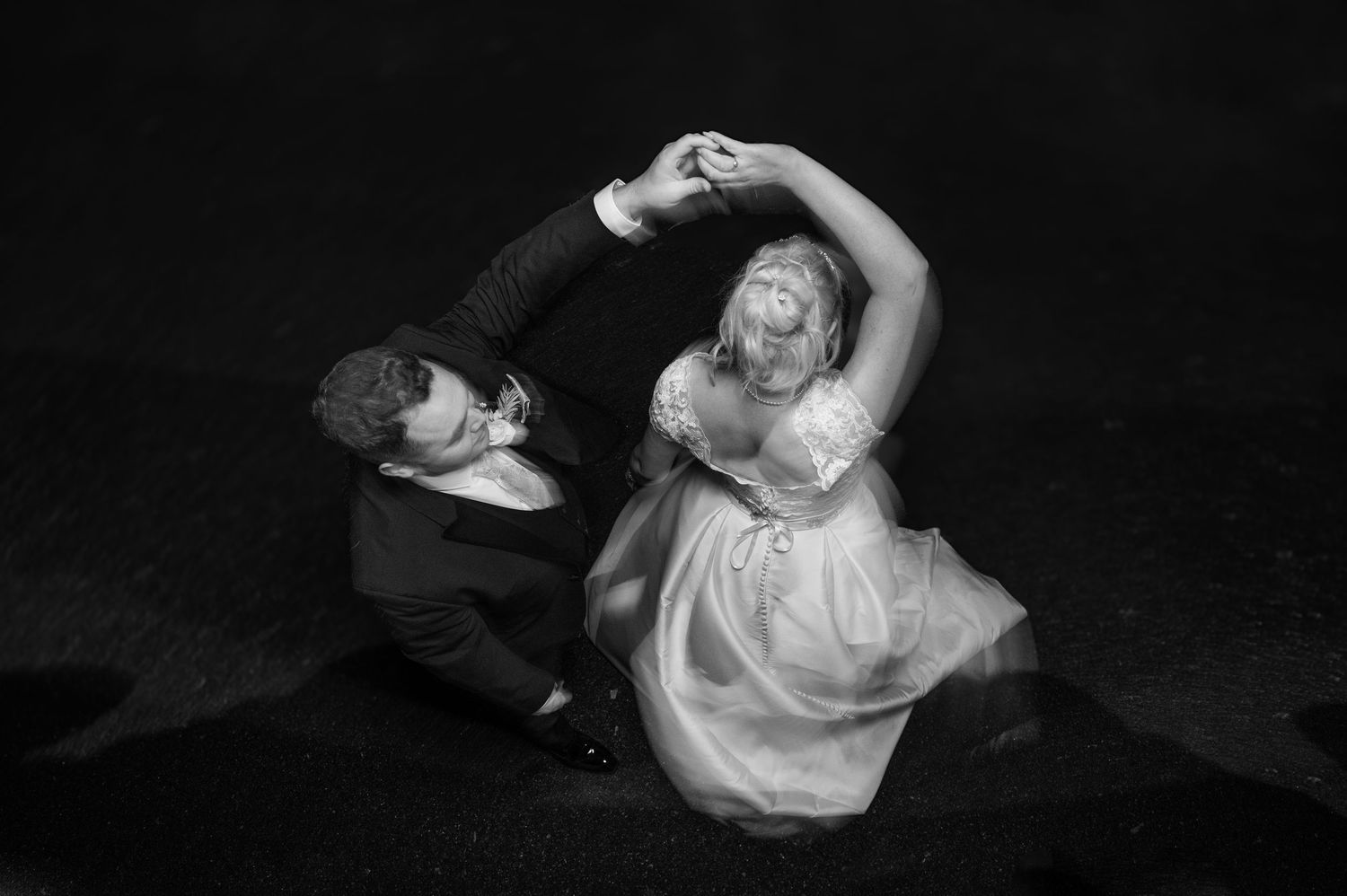 Black and white artistic photo of bride and groom dancing together on the floor.