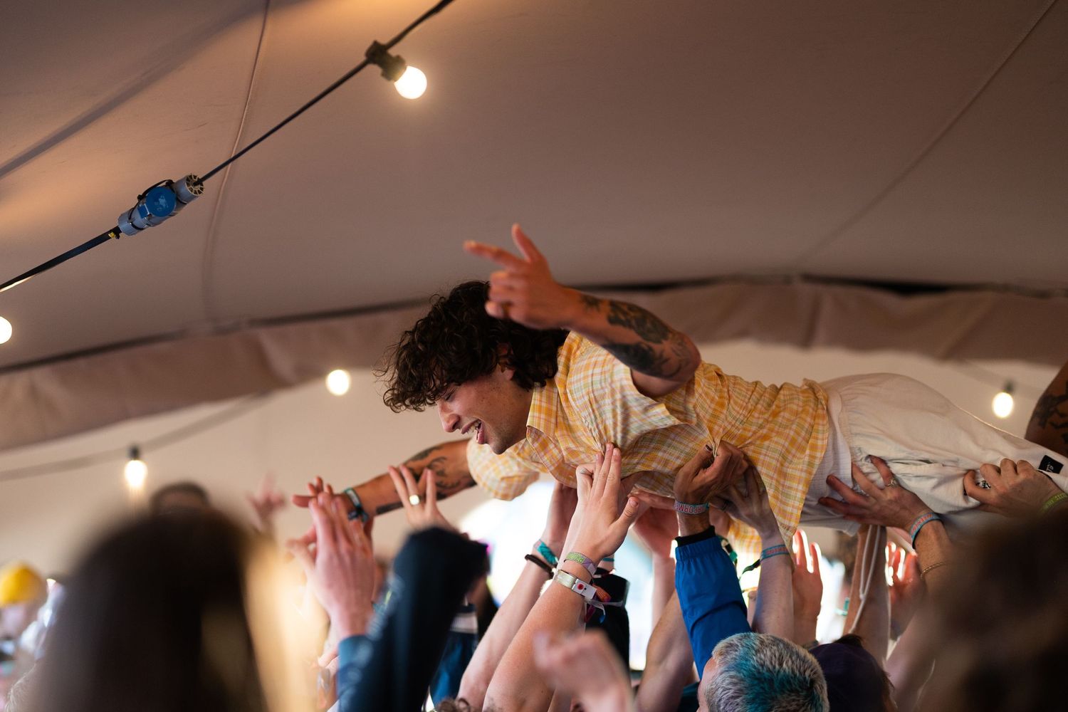 Tattooed performer crowd surfing over audience inside a tent at a live music festival.