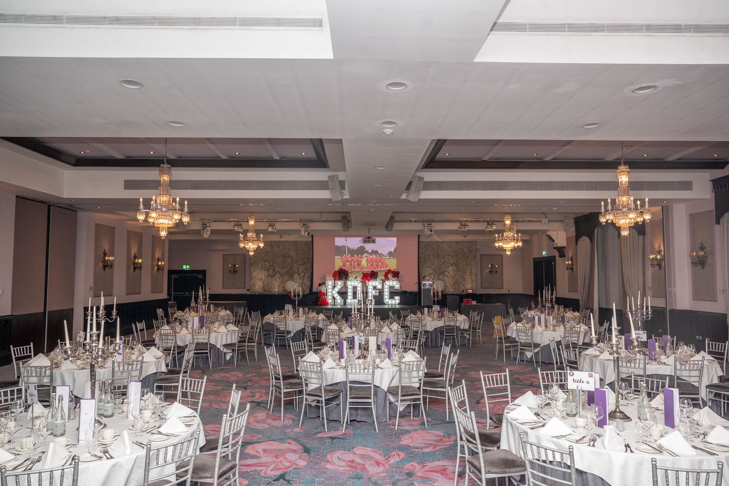 Elegant banquet hall with silver chiavari chairs and KDFC illuminated letters at formal gala.