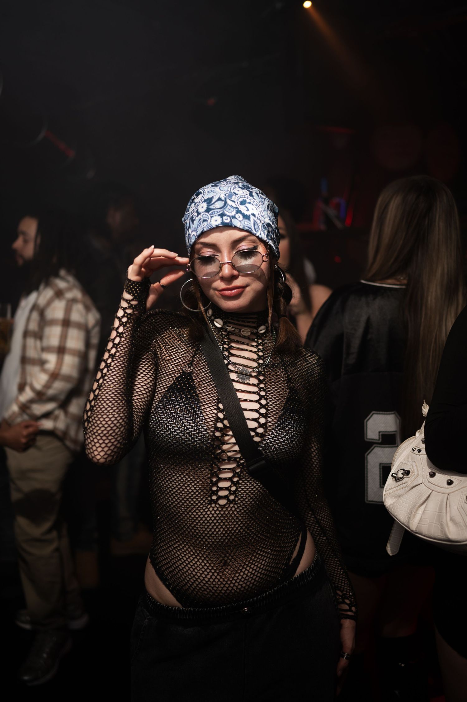 Woman in a mesh outfit and bandana posing at a dark nightclub event.