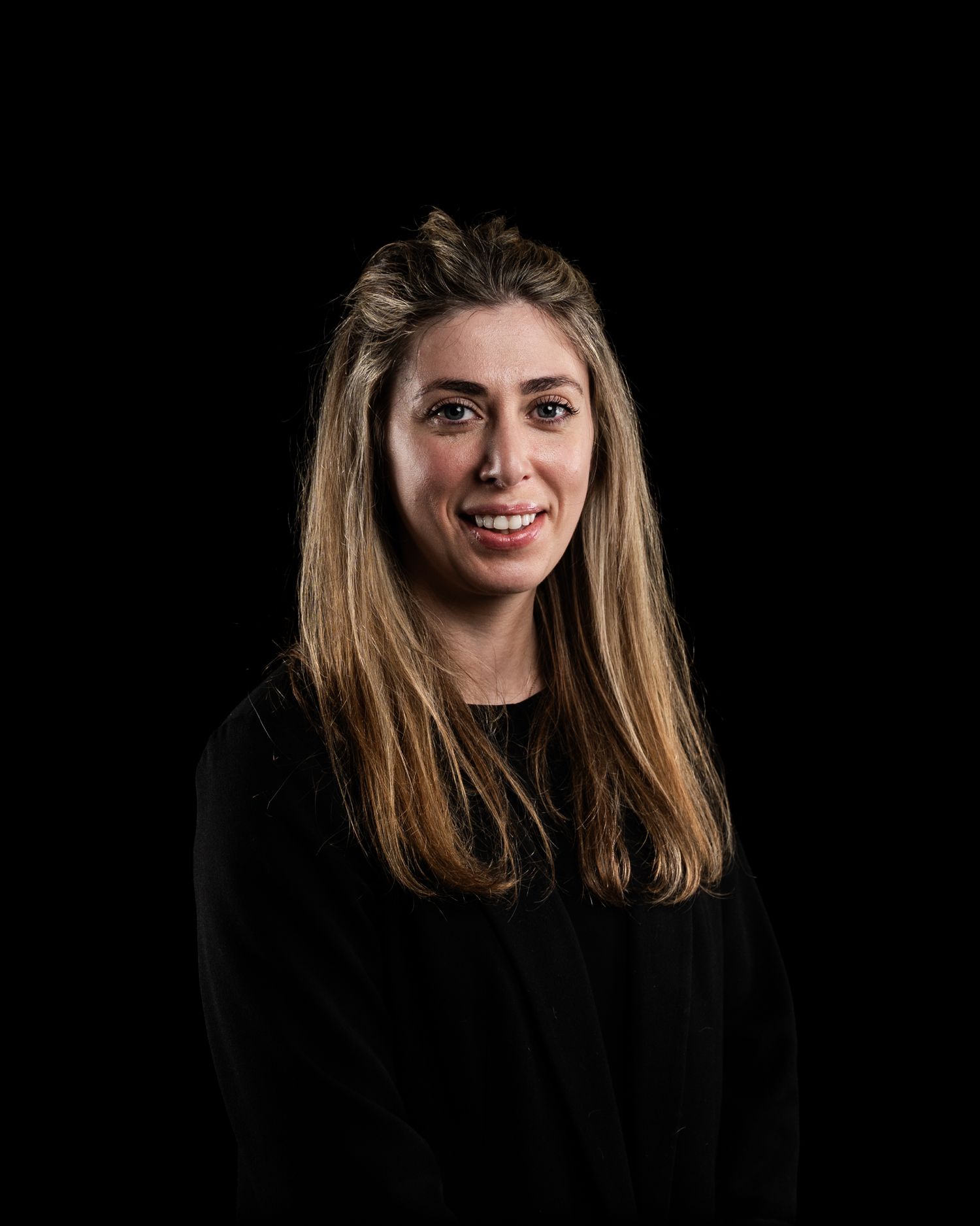 Professional headshot of a woman with long blonde highlighted hair wearing a black blazer against a dark background.