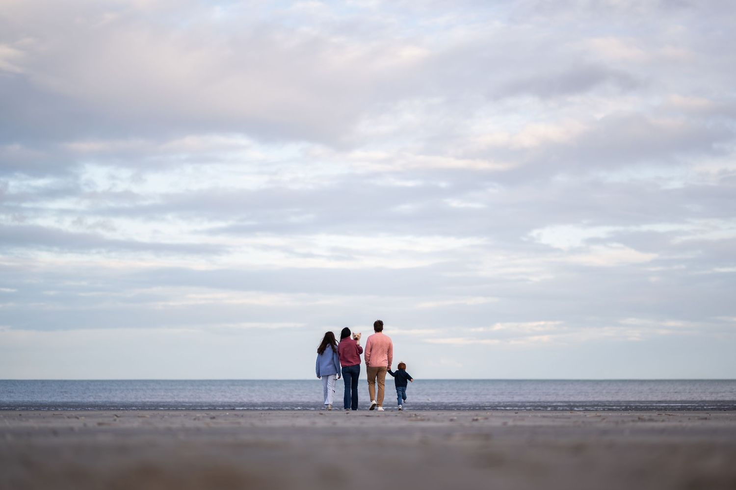 Family of four standing together on a beach at dusk, gazing at the ocean under a cloudy sky.