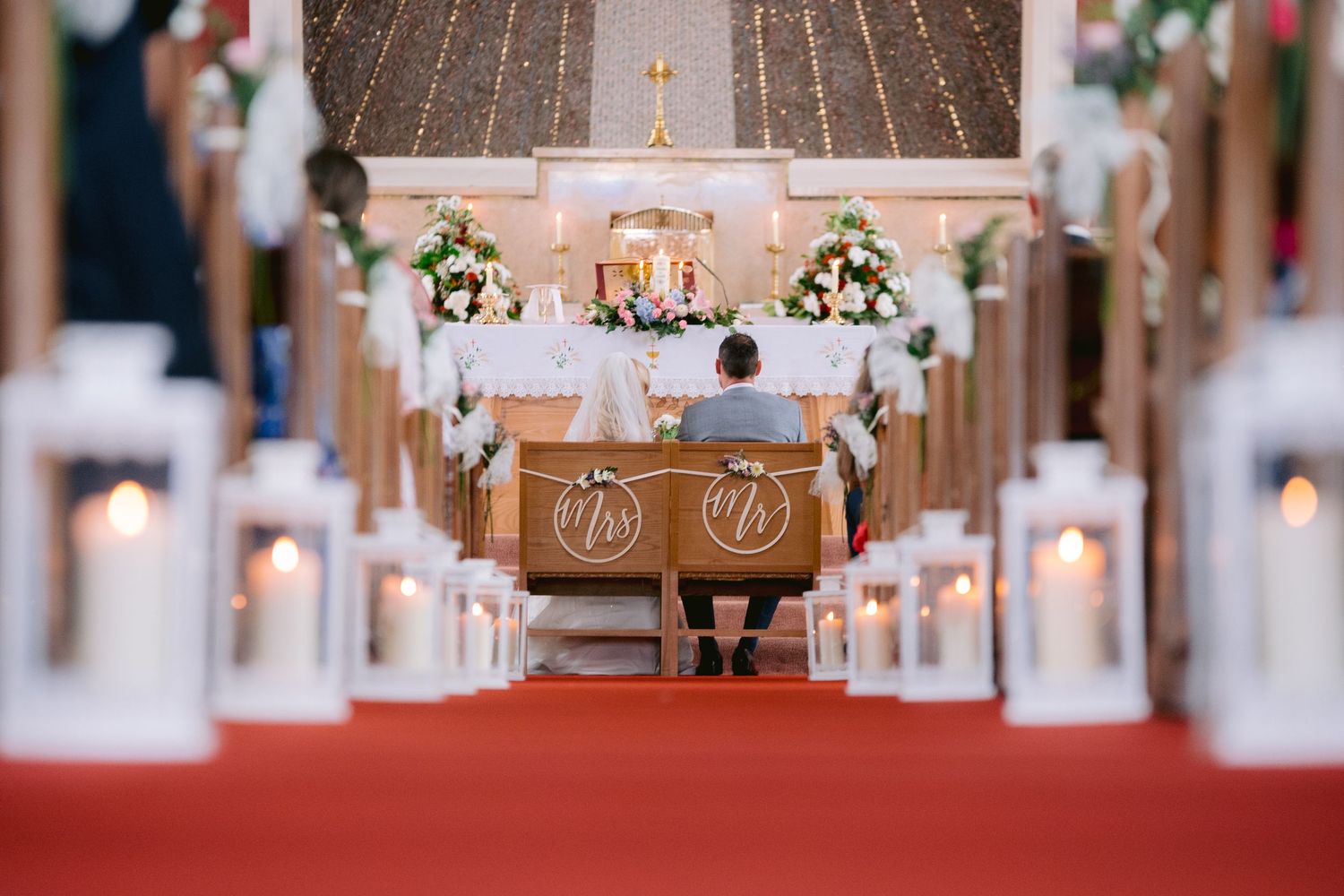 Church wedding ceremony aisle lined with candle lanterns leading to couple at the altar.