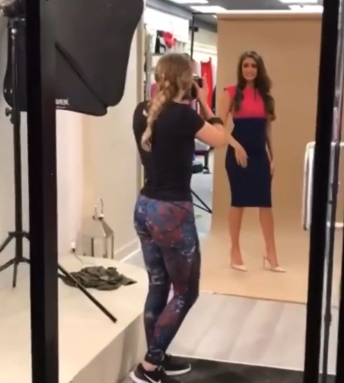 Female photographer shooting a model in a colorful dress during a professional fashion photo shoot indoors.