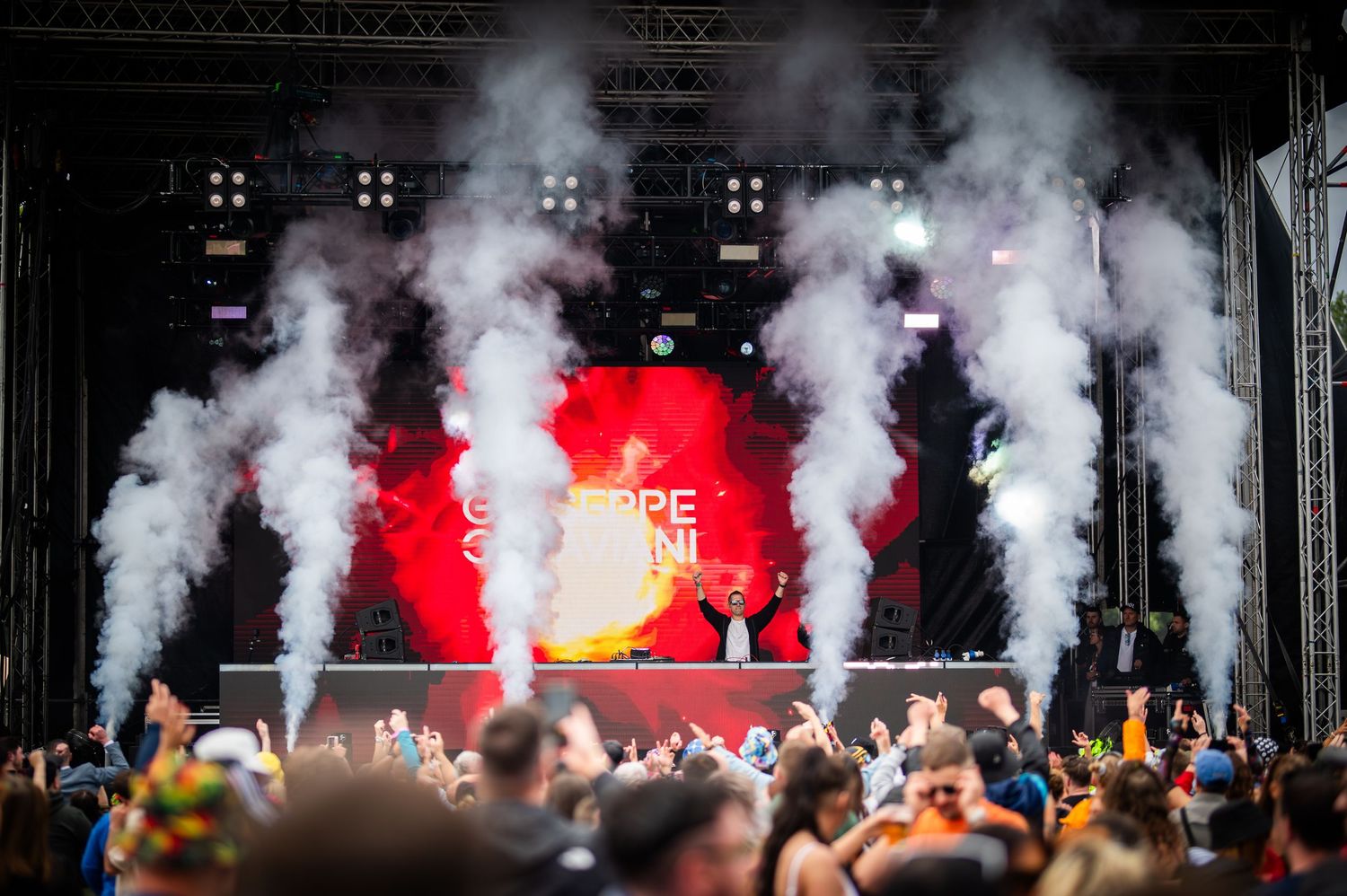 DJ Giuseppe Ottaviani performing on a smoke-filled festival stage before a massive crowd.