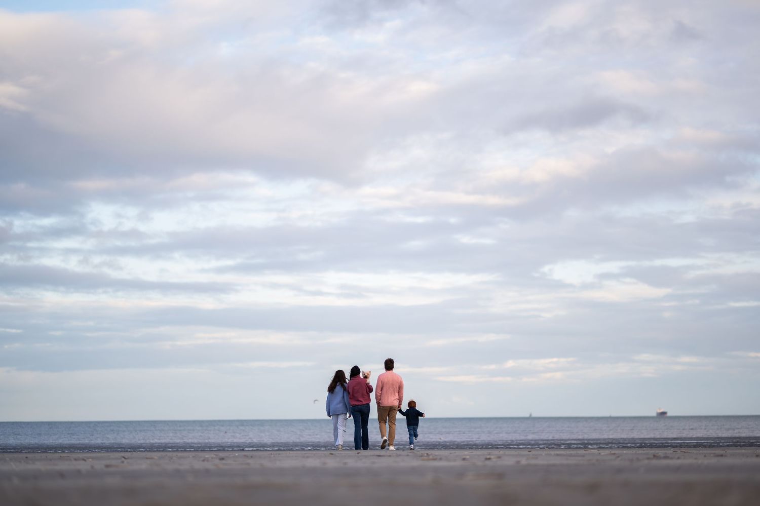 Family of four holding hands while standing on a beach at dusk under a cloudy sky.