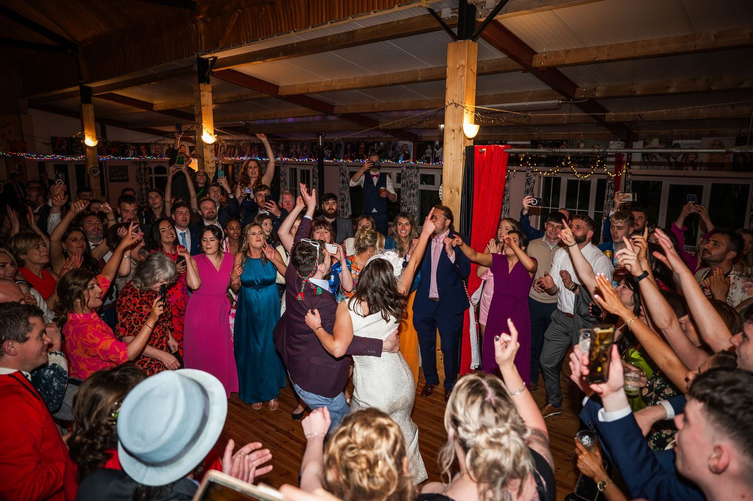 Energetic wedding reception crowd dancing and raising hands on the dance floor.