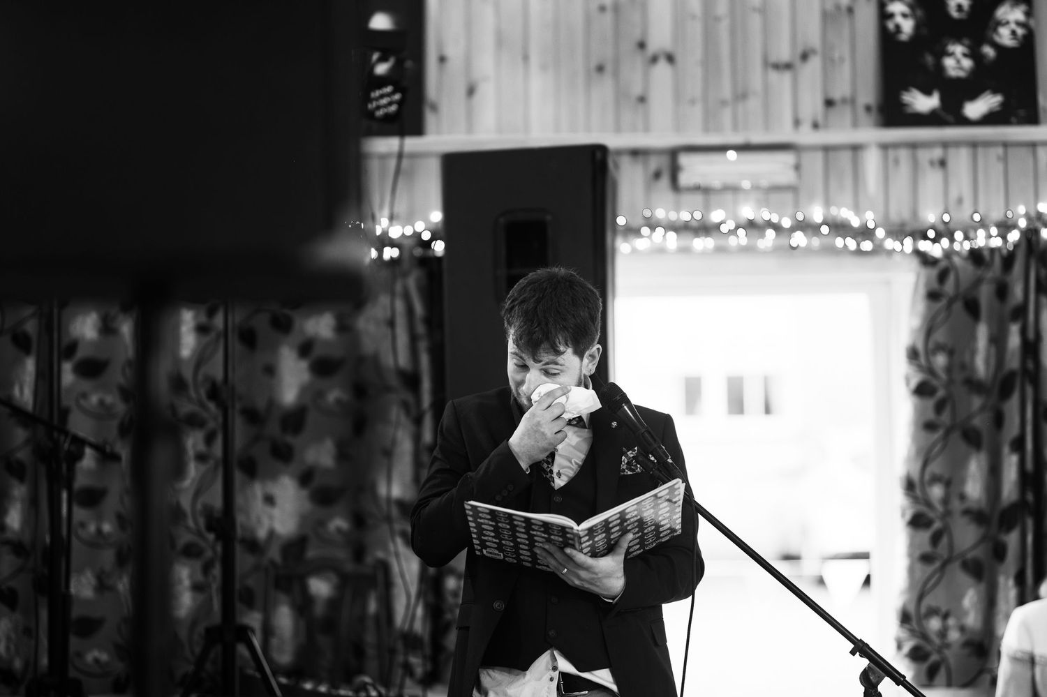 Black and white photo of a man reading at a microphone during a wedding speech.