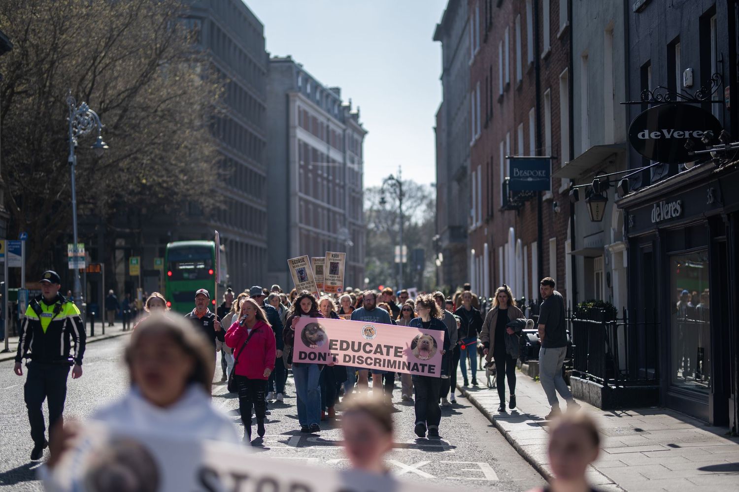 Protesters march down a city street holding an Educate Down Syndrome banner on a sunny day.