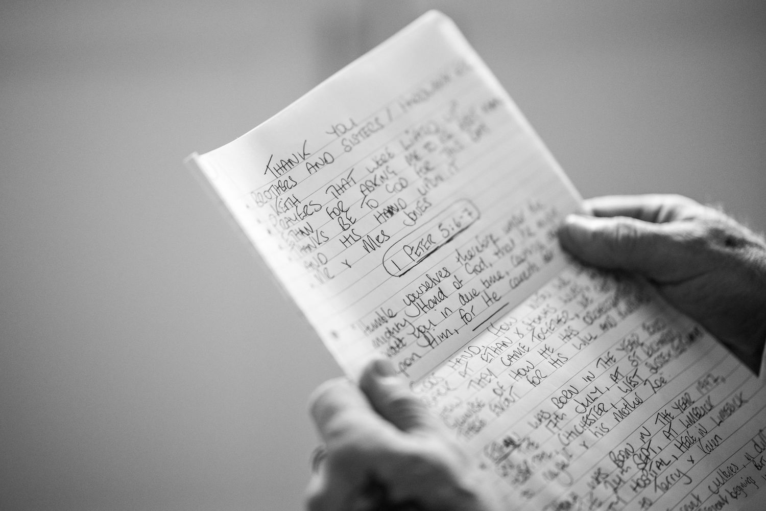 Hands holding a handwritten notebook filled with dense notes and calculations in black and white.