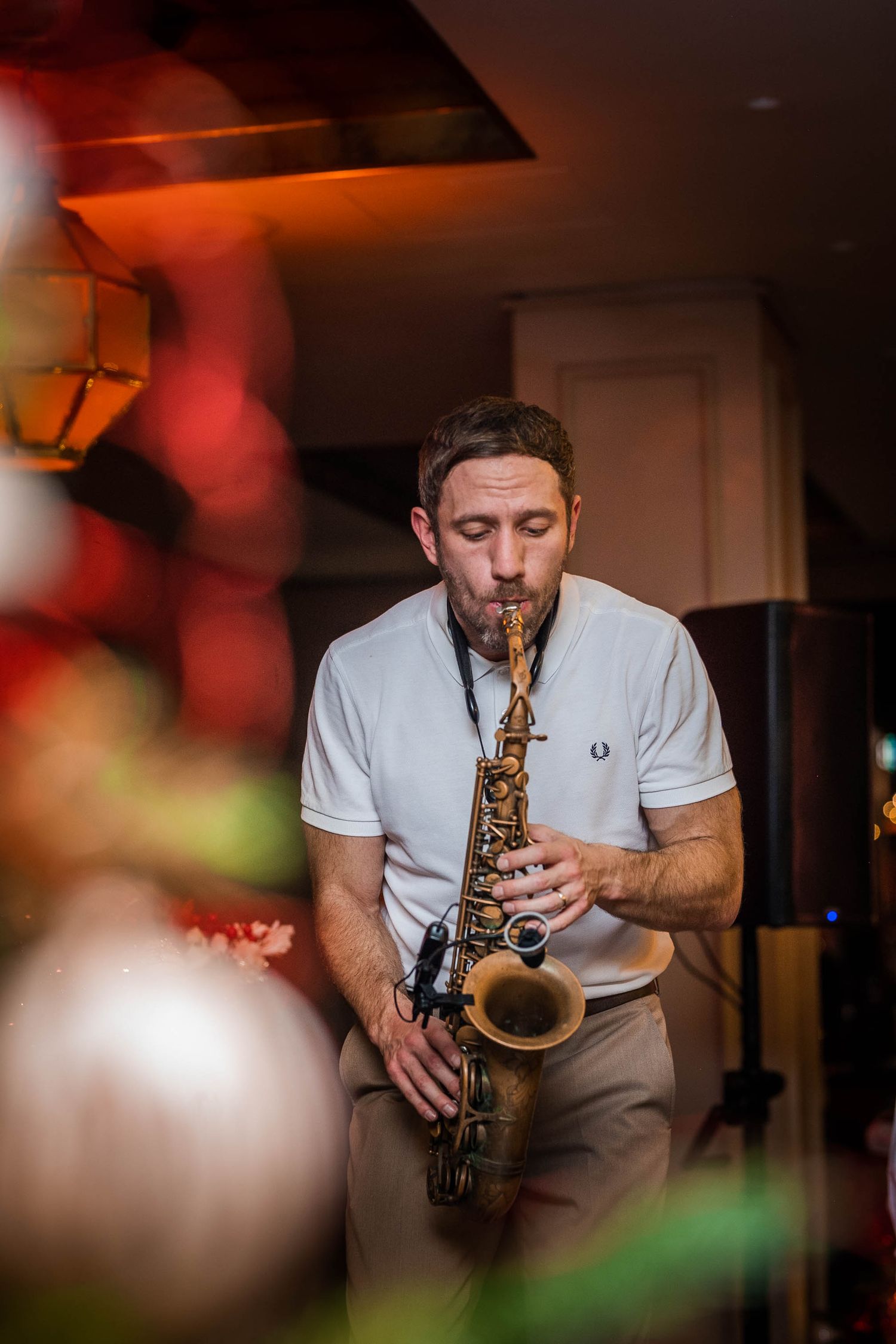 Male musician playing saxophone at intimate indoor venue with warm red ambient lighting.