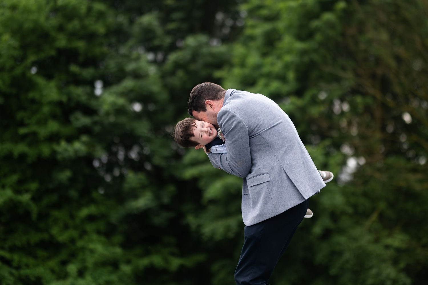 Golfer in gray blazer bending forward after swing on lush green golf course.