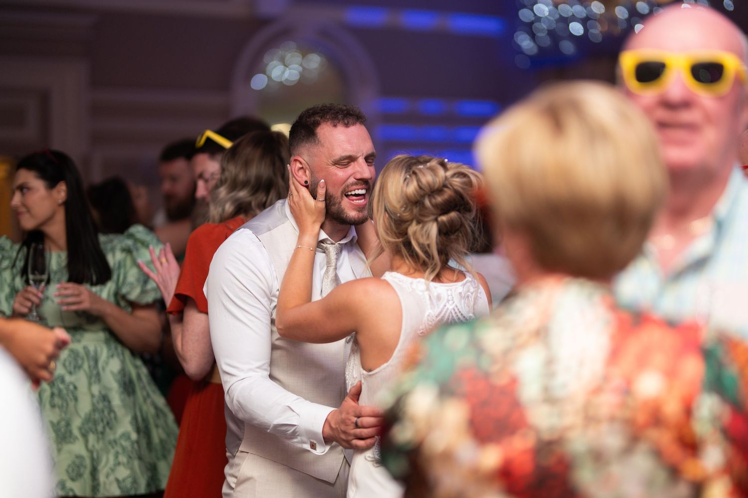 Bride and groom sharing first dance surrounded by guests at lively wedding reception.