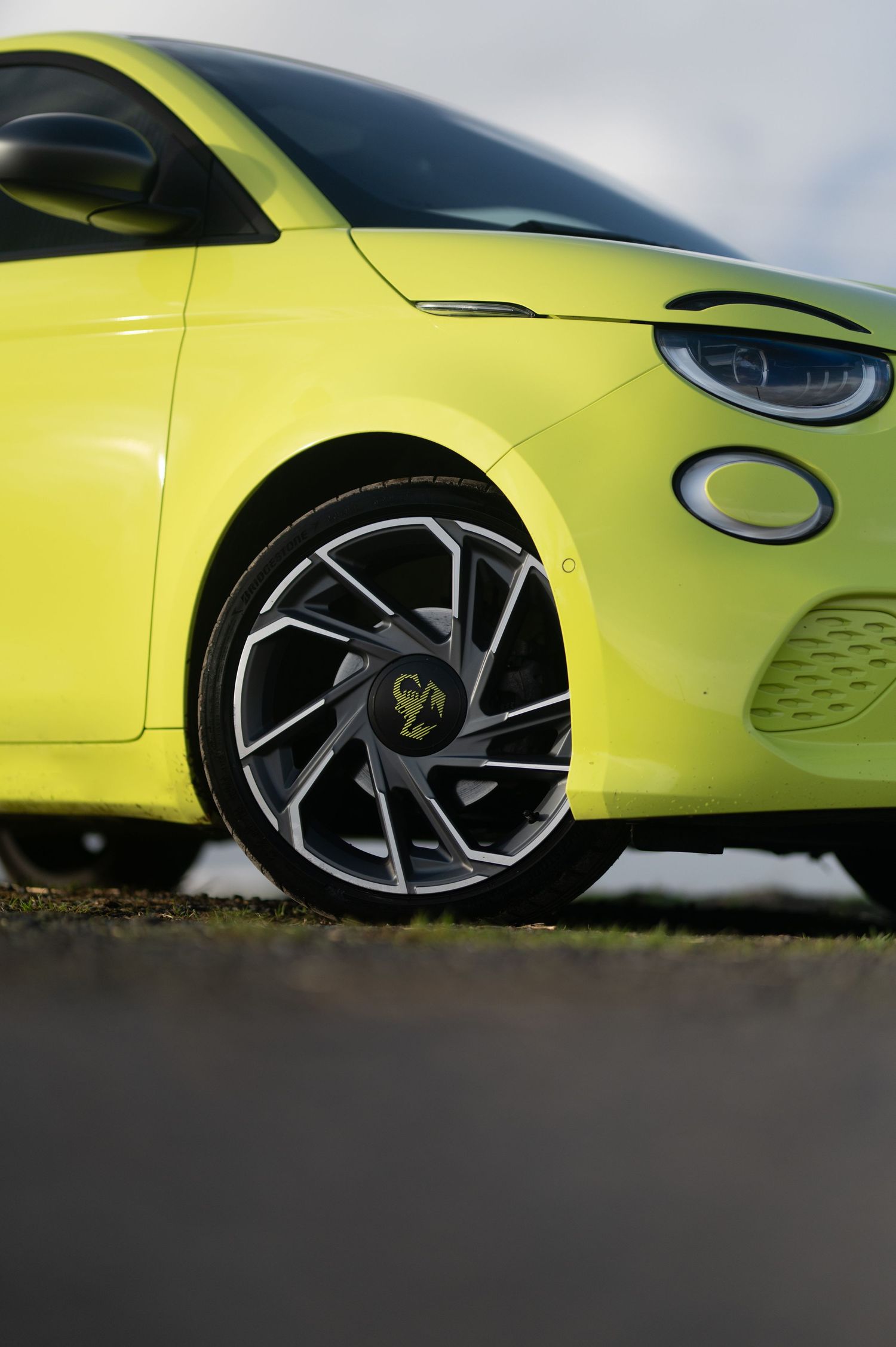 Bright yellow Fiat 500 electric car with stylish alloy wheels on a dark road.