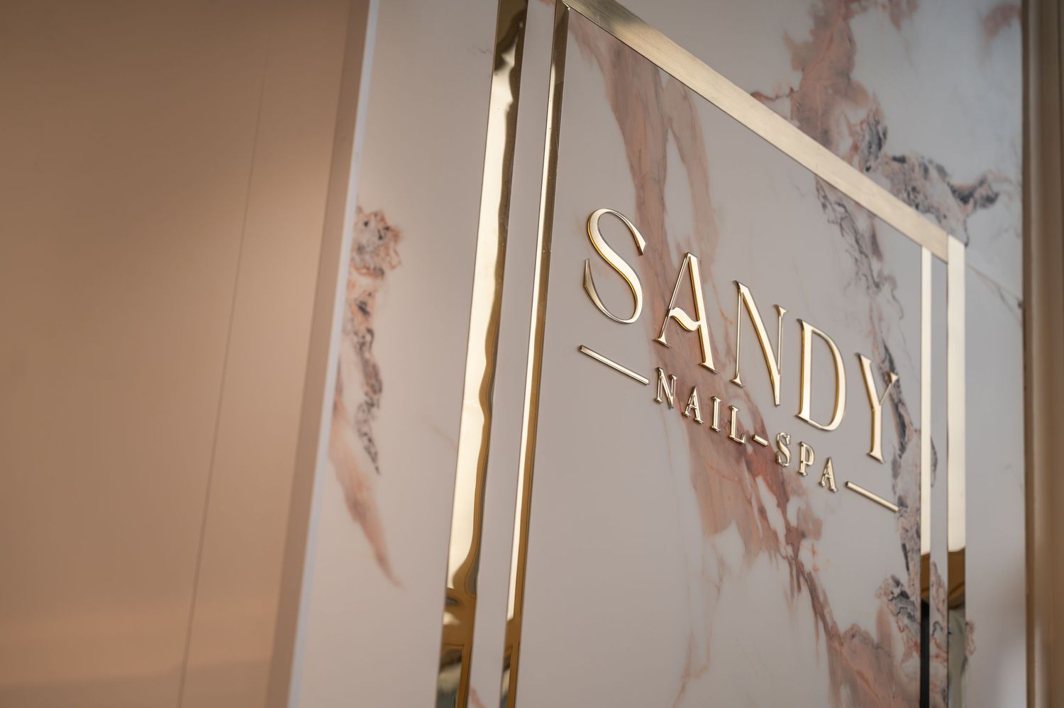Sandy Nail Spa elegant gold logo sign on marble background in luxury nail salon interior.