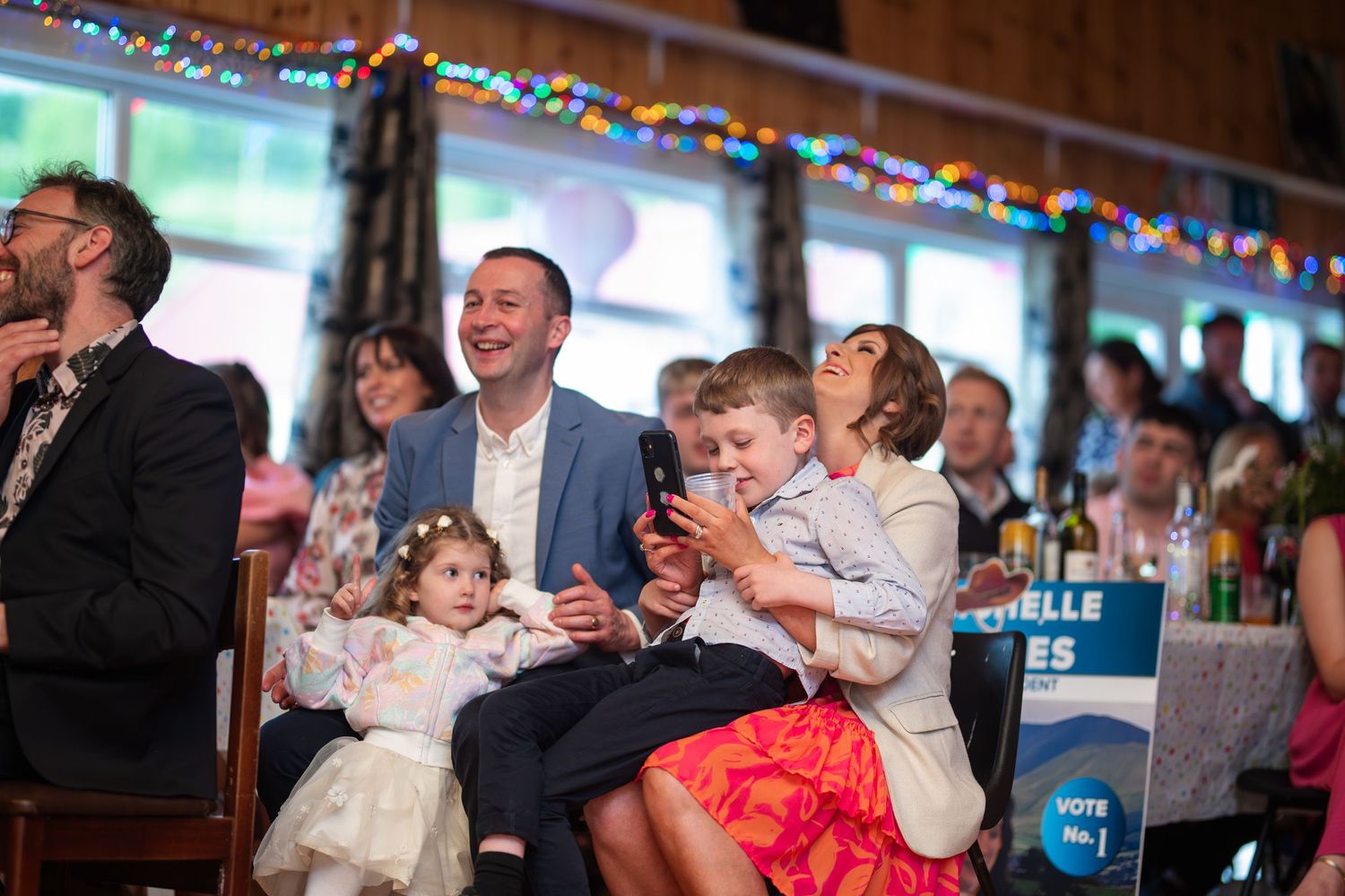 Family laughing together at a wedding reception with colorful fairy lights.