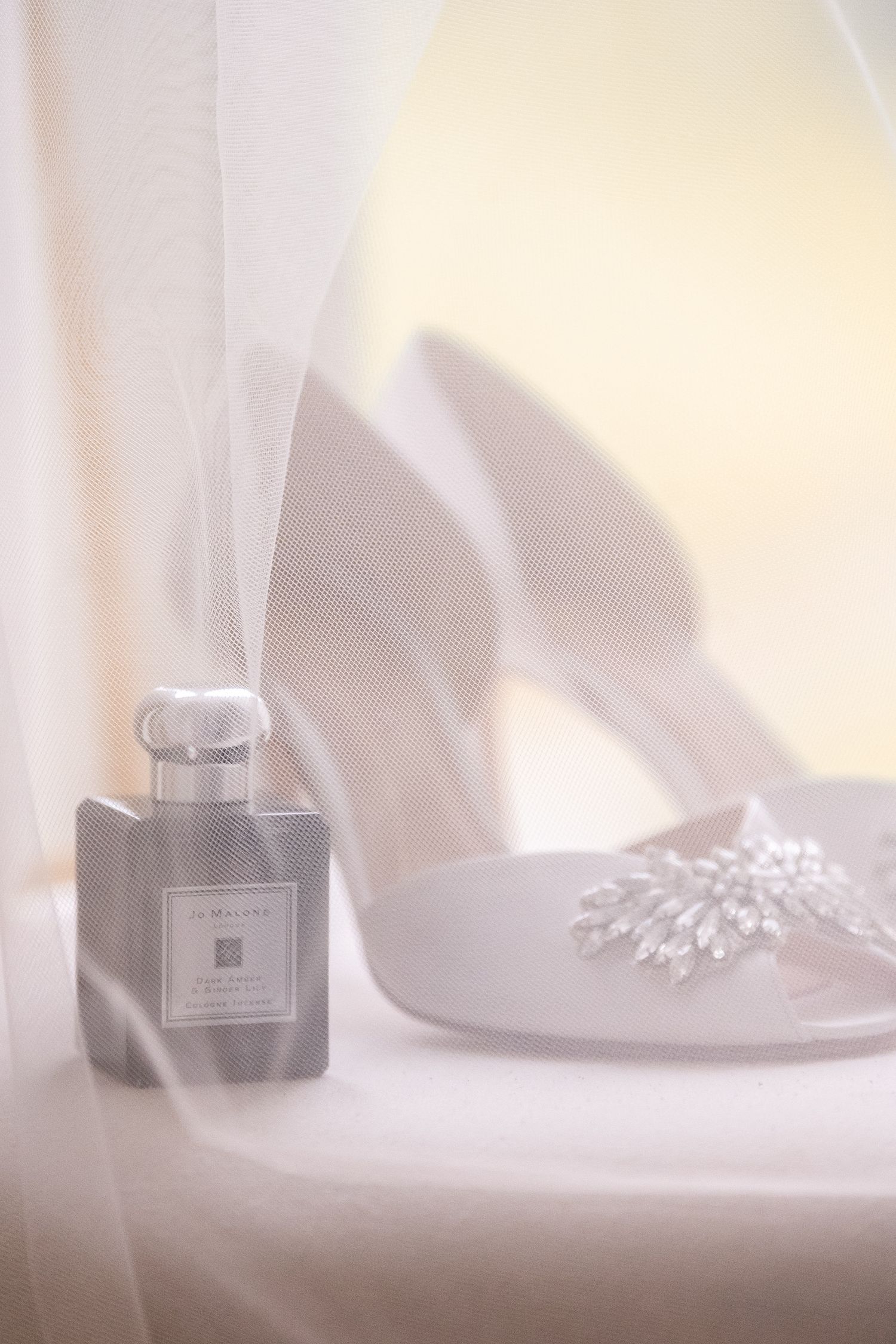 White bridal heels with crystal embellishment beside a Jo Malone perfume bottle.