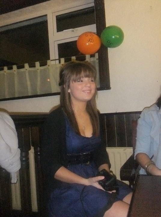 Young woman in a blue dress smiling at a party with orange and green balloons in the background.