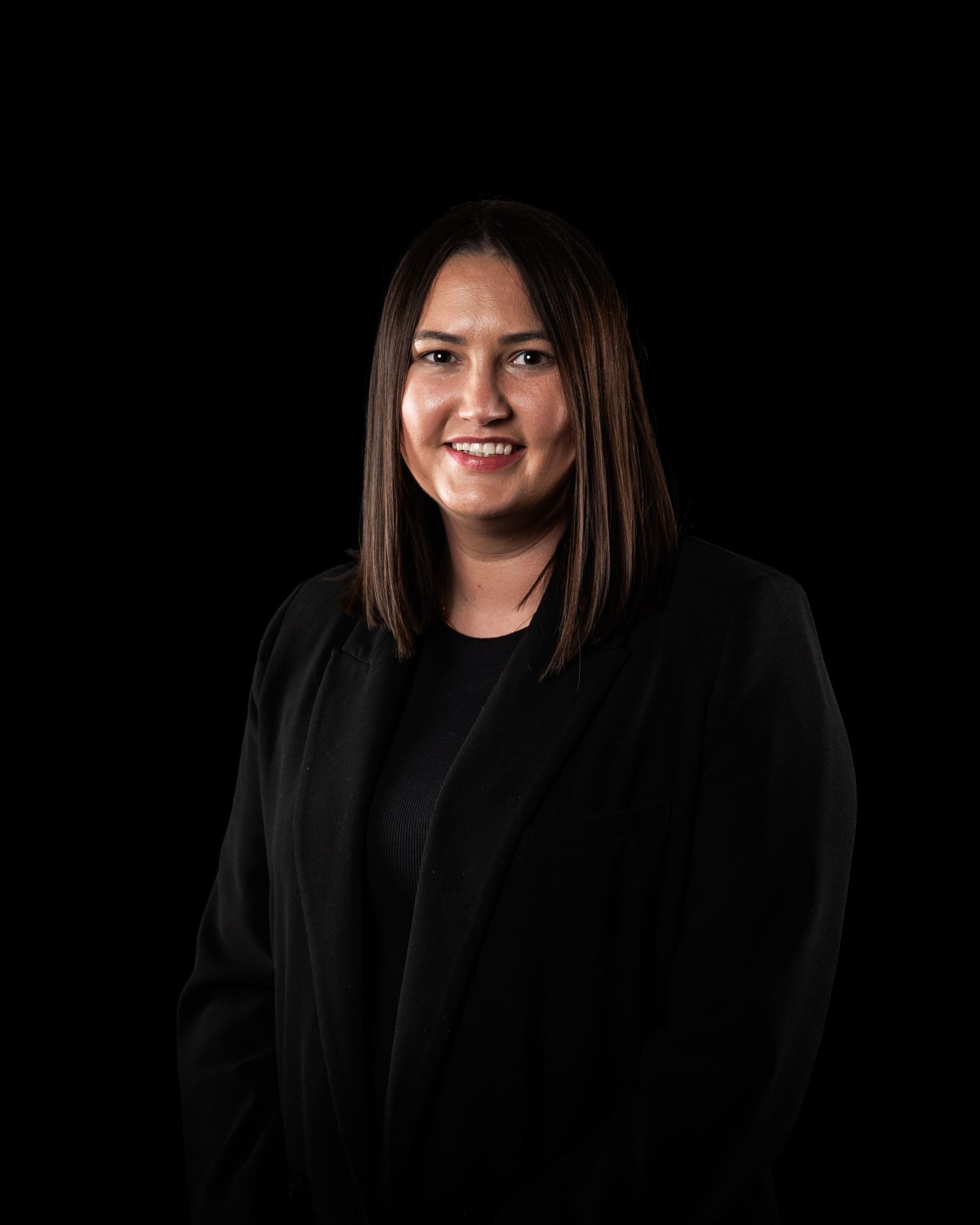 Professional headshot of a woman with straight dark hair wearing a black blazer against a dark background.