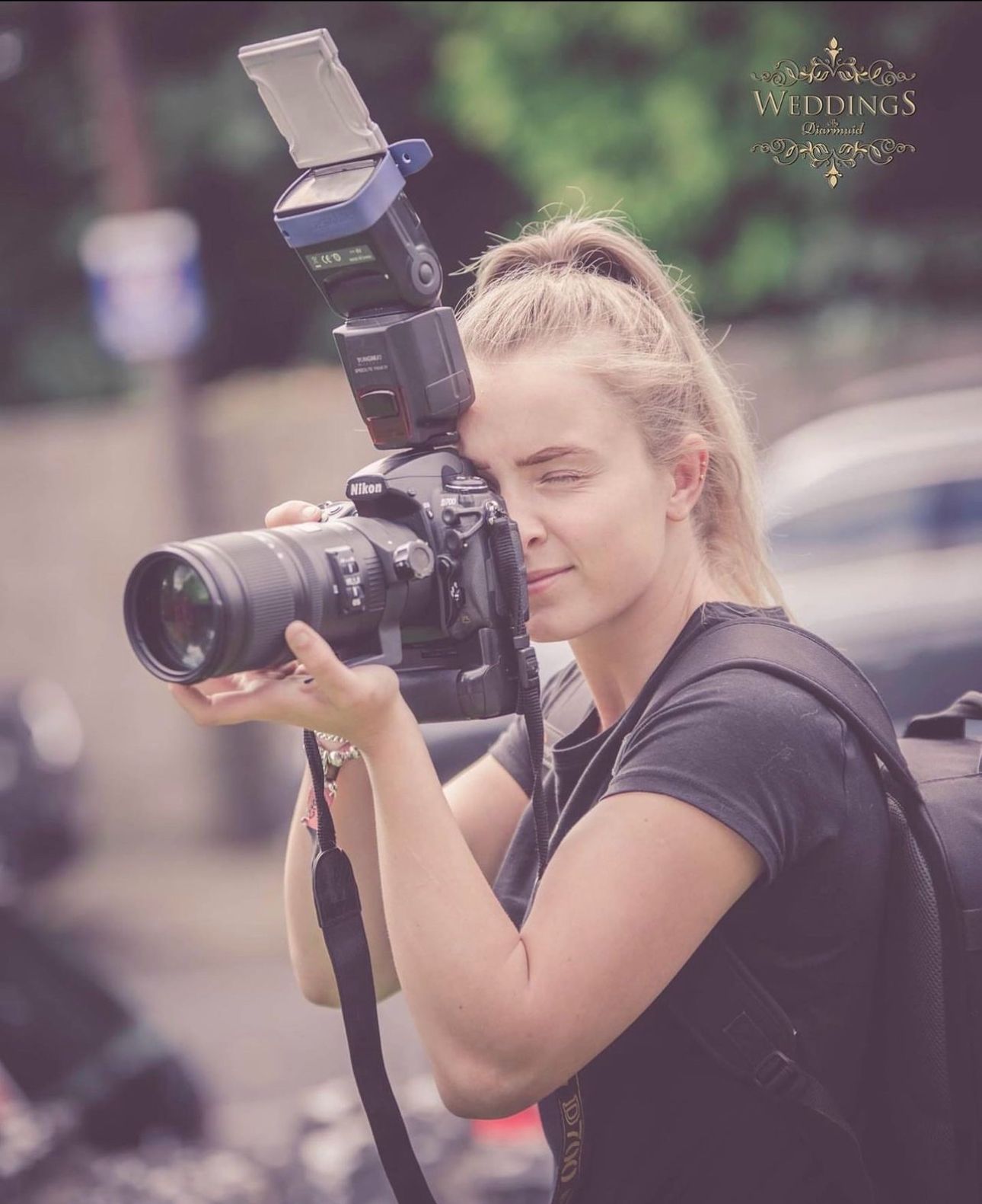 Young blonde female photographer focusing through a DSLR camera with flash at a weddings photography event.
