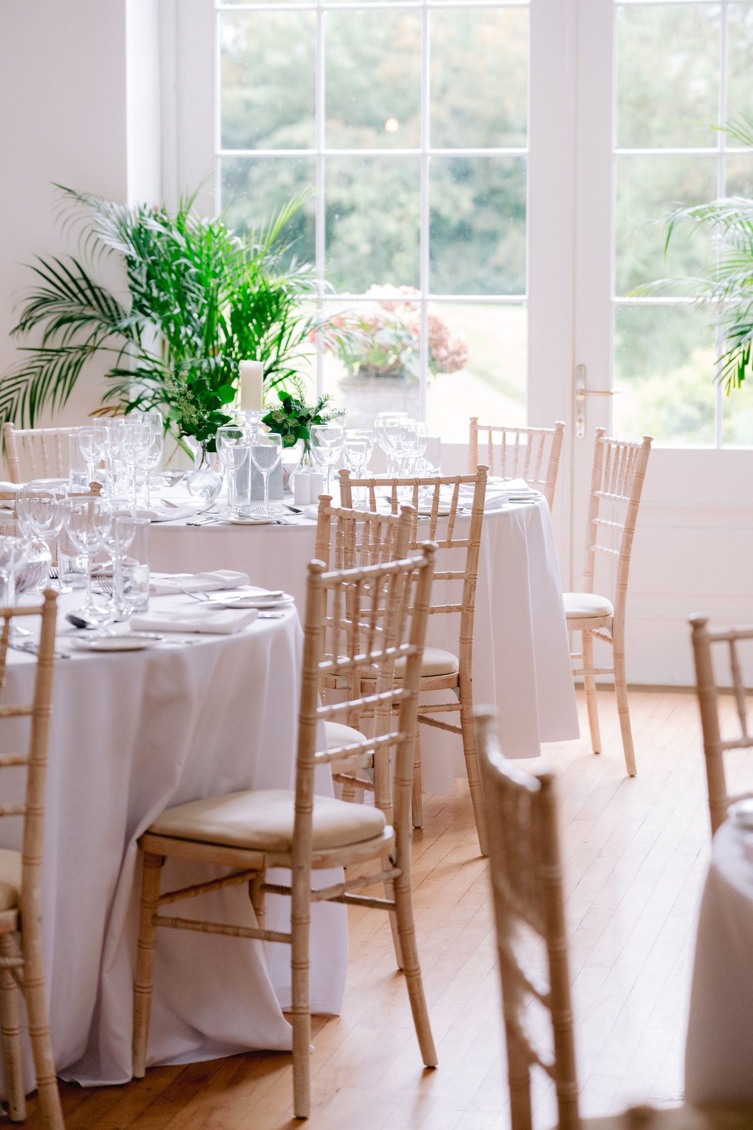 Bright wedding reception room with white tablecloths, chiavari chairs, and lush green centerpieces.