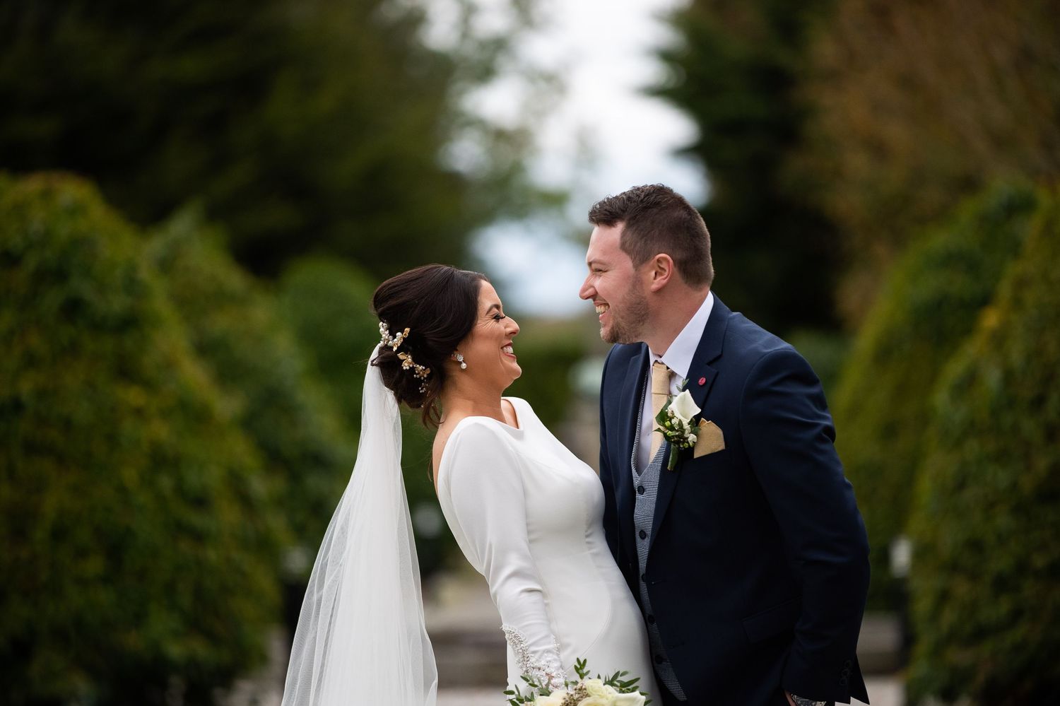 Bride and groom share a romantic moment in a lush garden, bride wearing a white gown and veil.