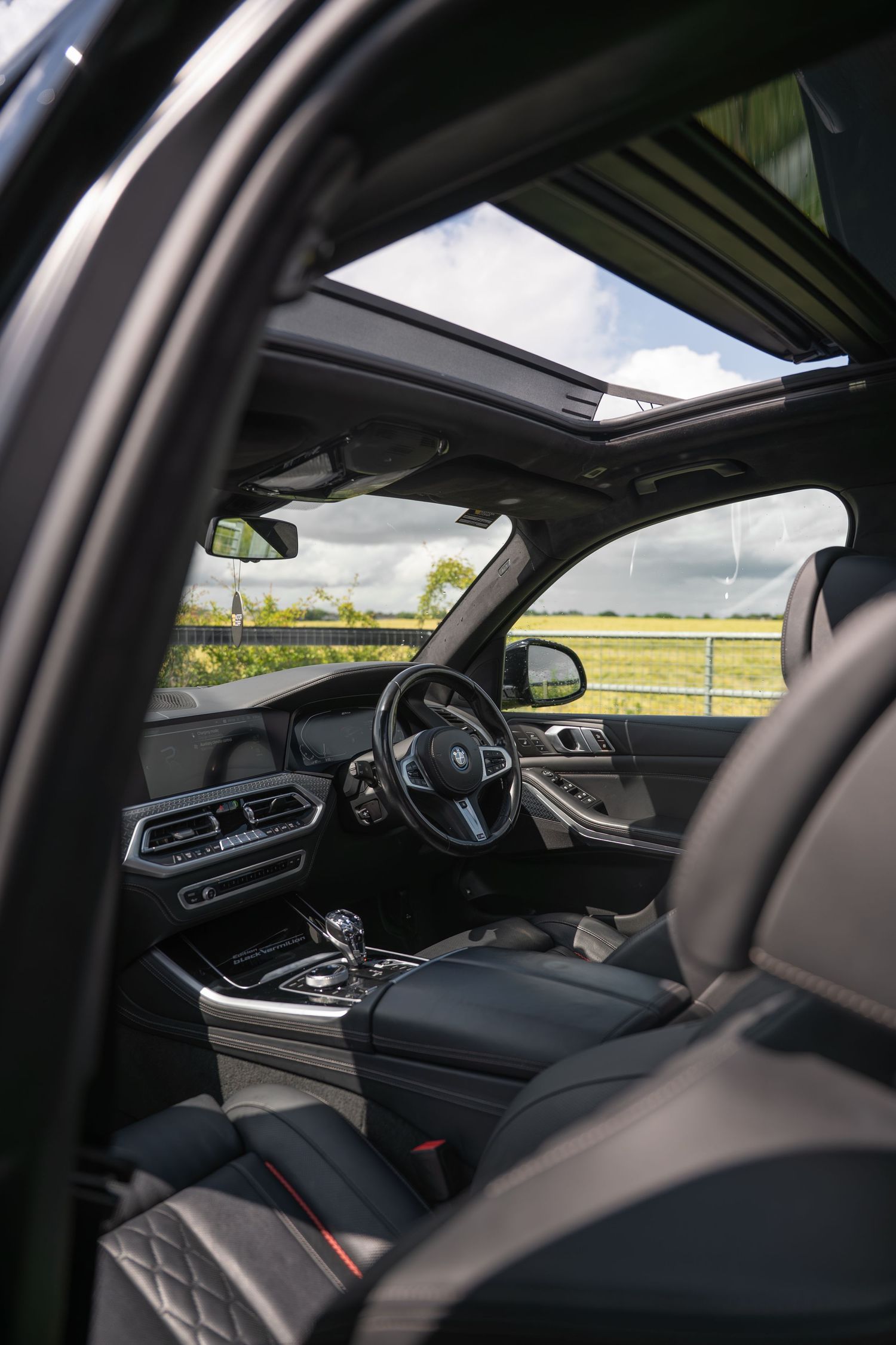 Luxury BMW SUV interior with panoramic sunroof, leather seats, and dashboard controls.