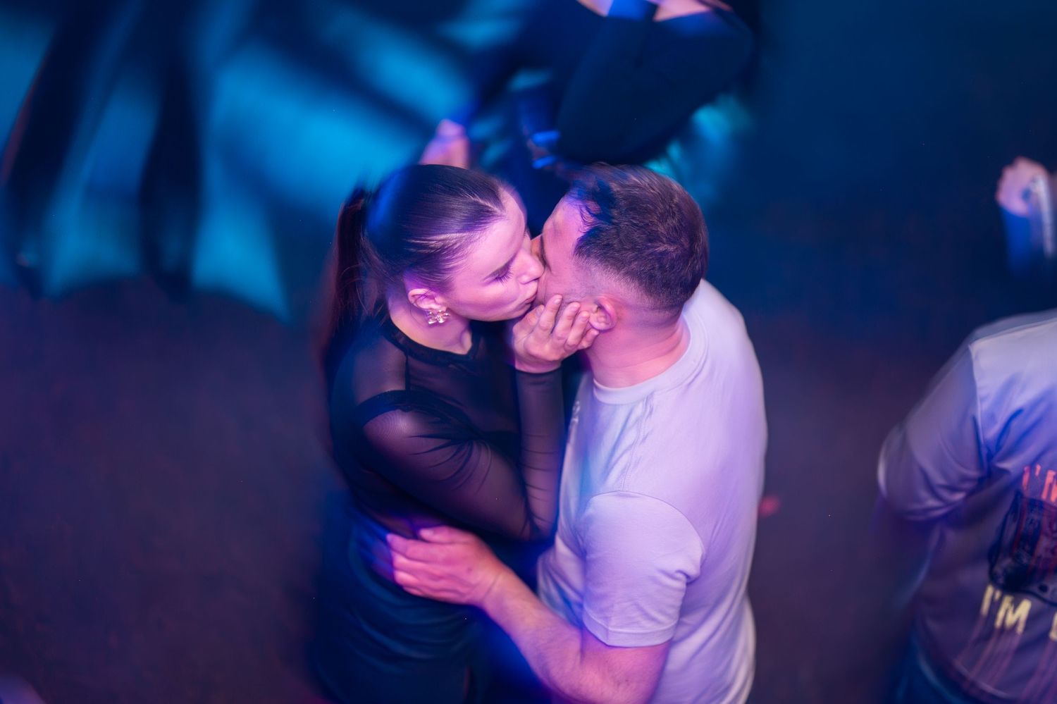 A couple sharing a romantic kiss on a dimly lit blue-lit dance floor.