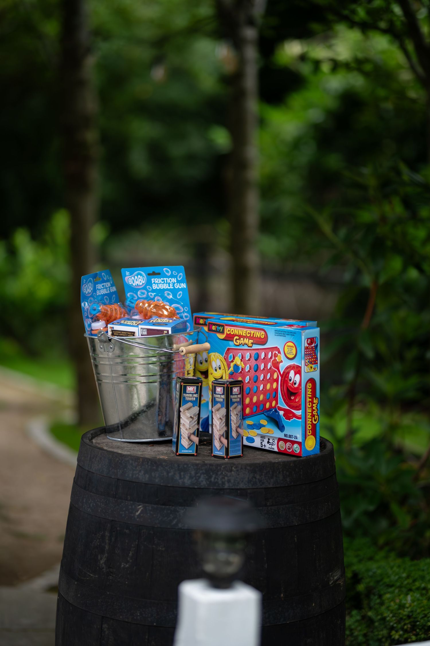 Outdoor wedding lawn games display on a barrel including Connect Four and bubble wands in lush garden setting.