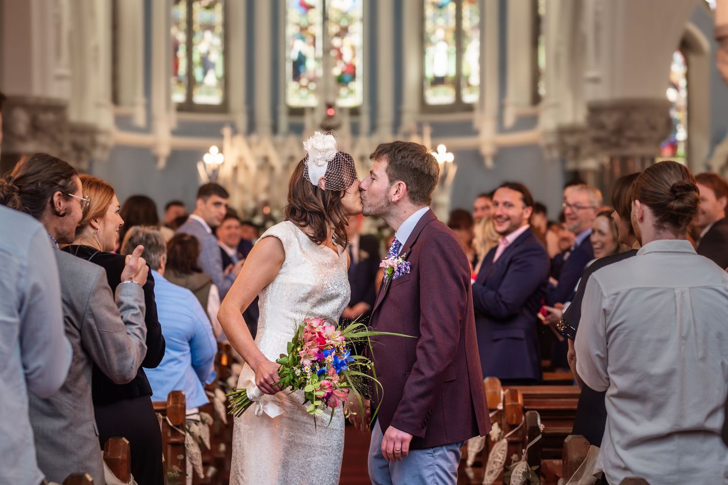 Bride and groom share a first kiss at the church altar surrounded by wedding guests during a traditional ceremony.