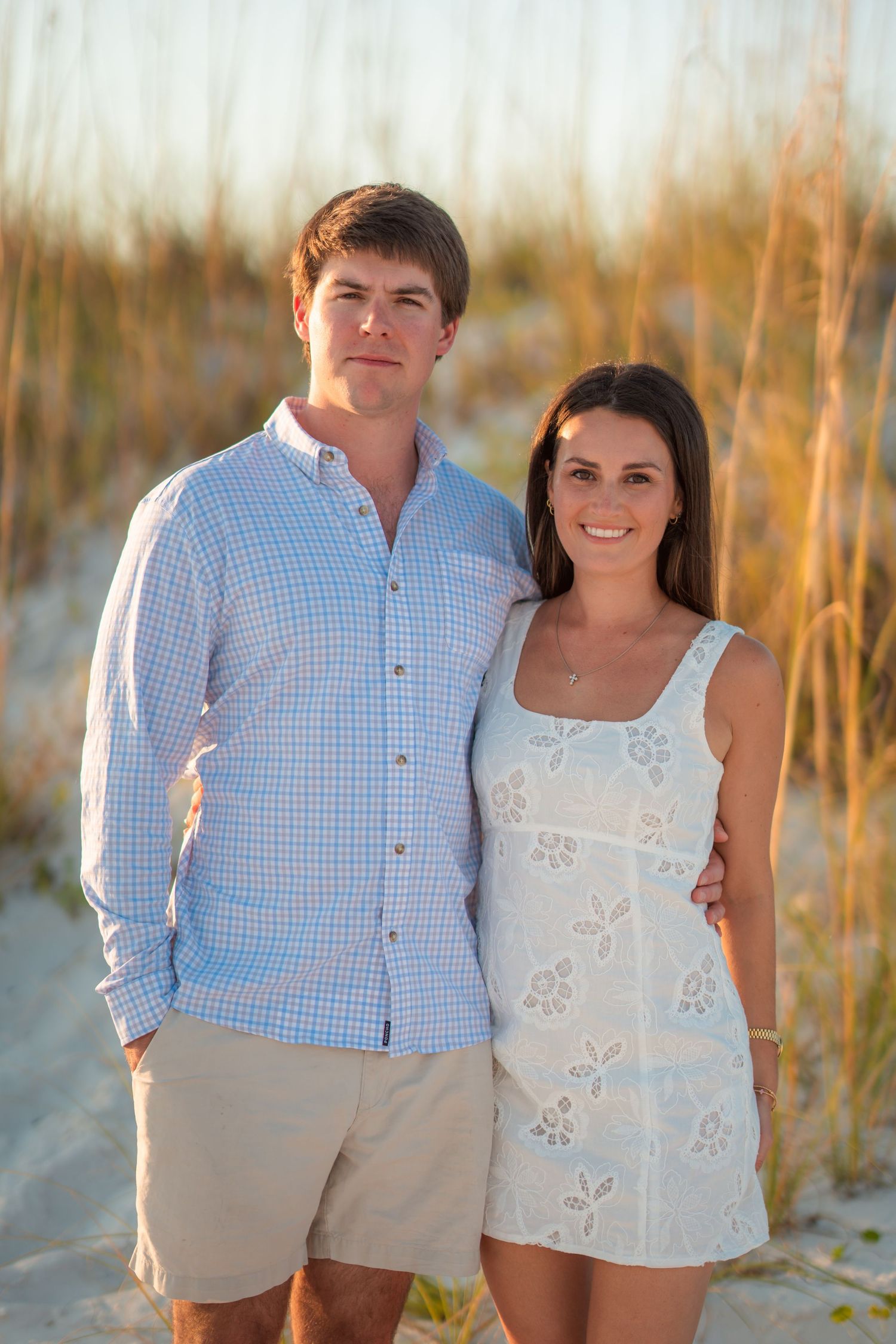 Couple in coordinated blue and white outfits posing on beach with sea grass.