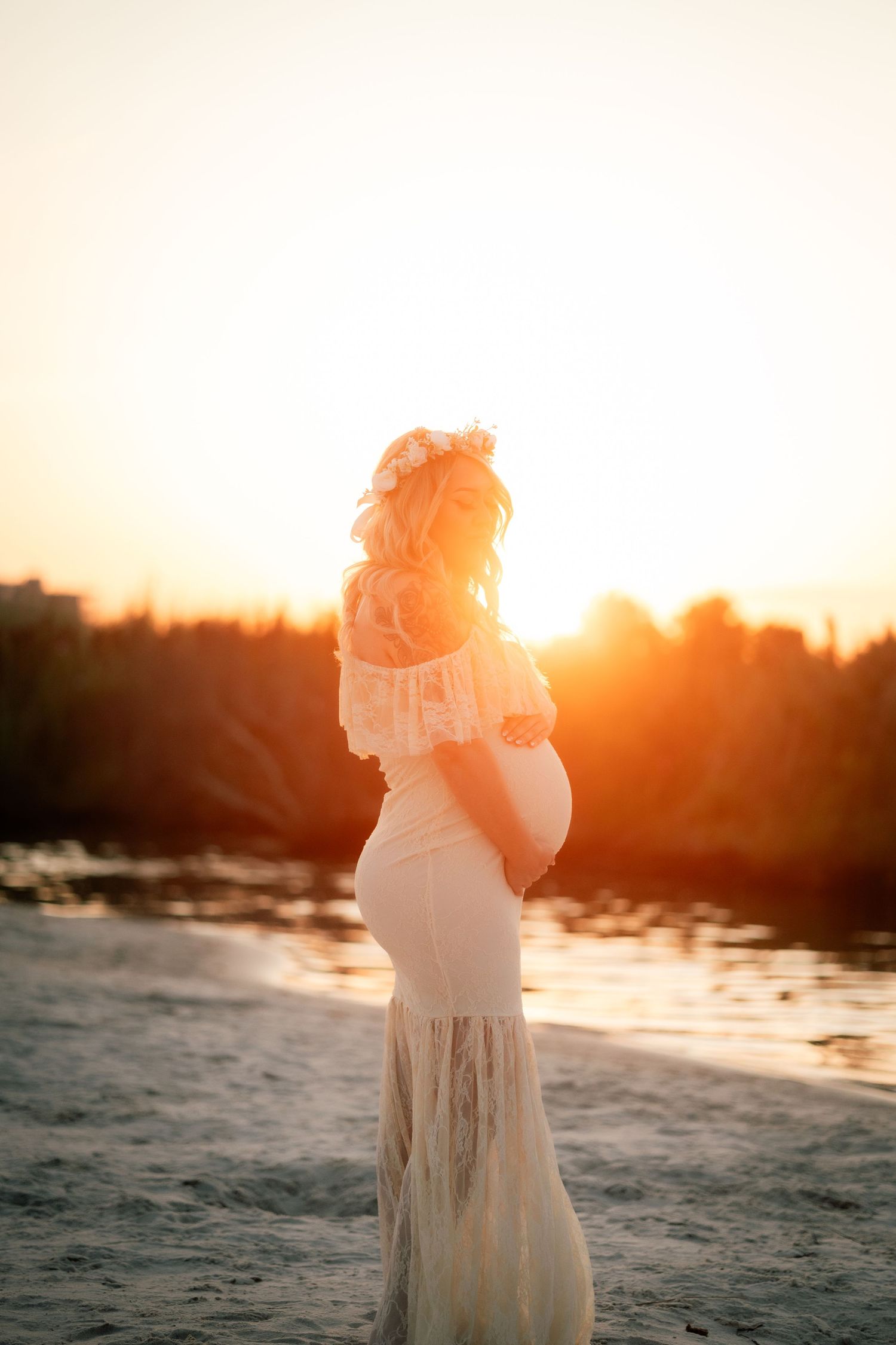 A silhouette of a figure in flowing dress stands against a dramatic sunset on the beach.