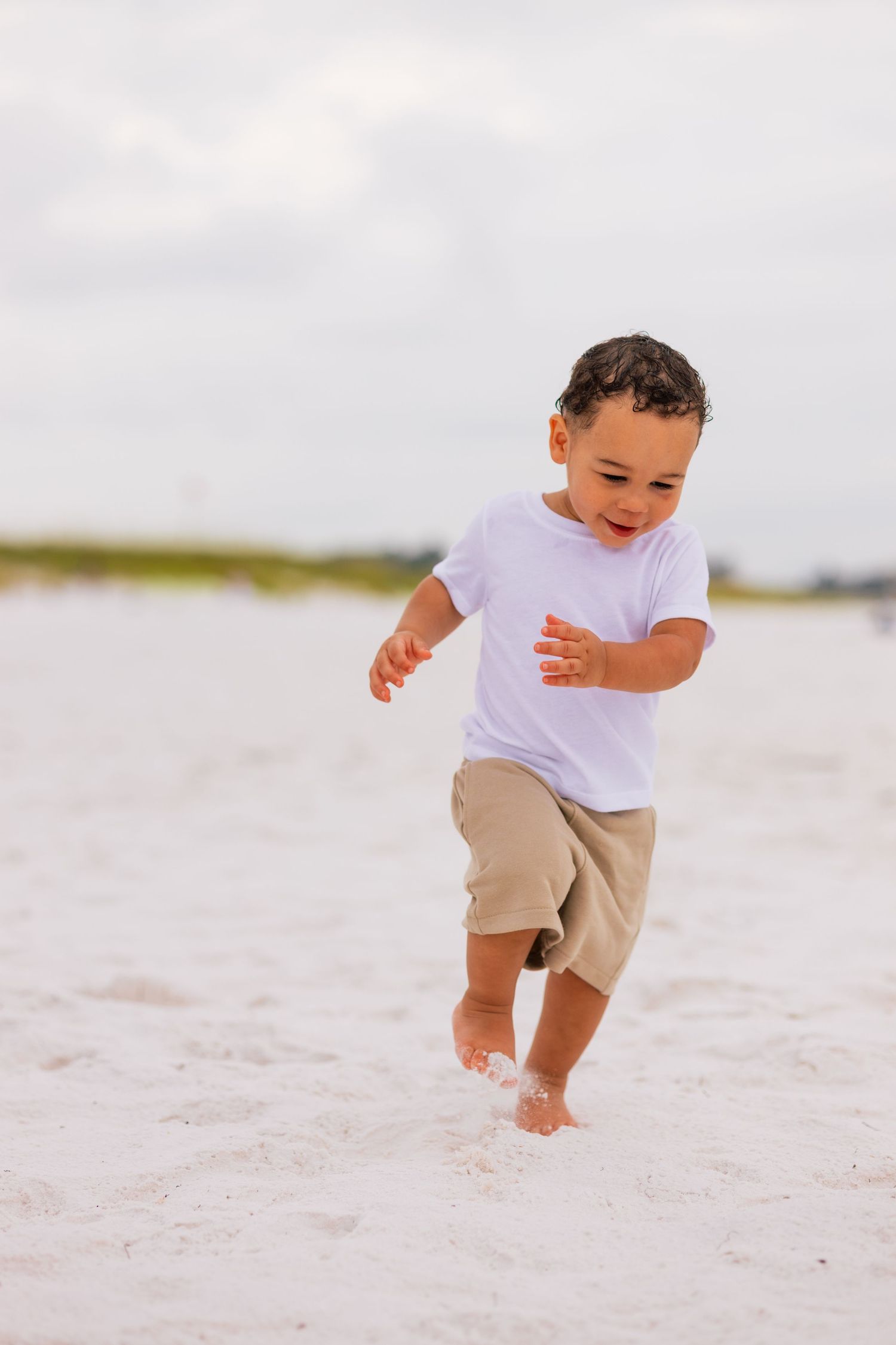 A child in white and khaki plays joyfully in the white sand at the beach.