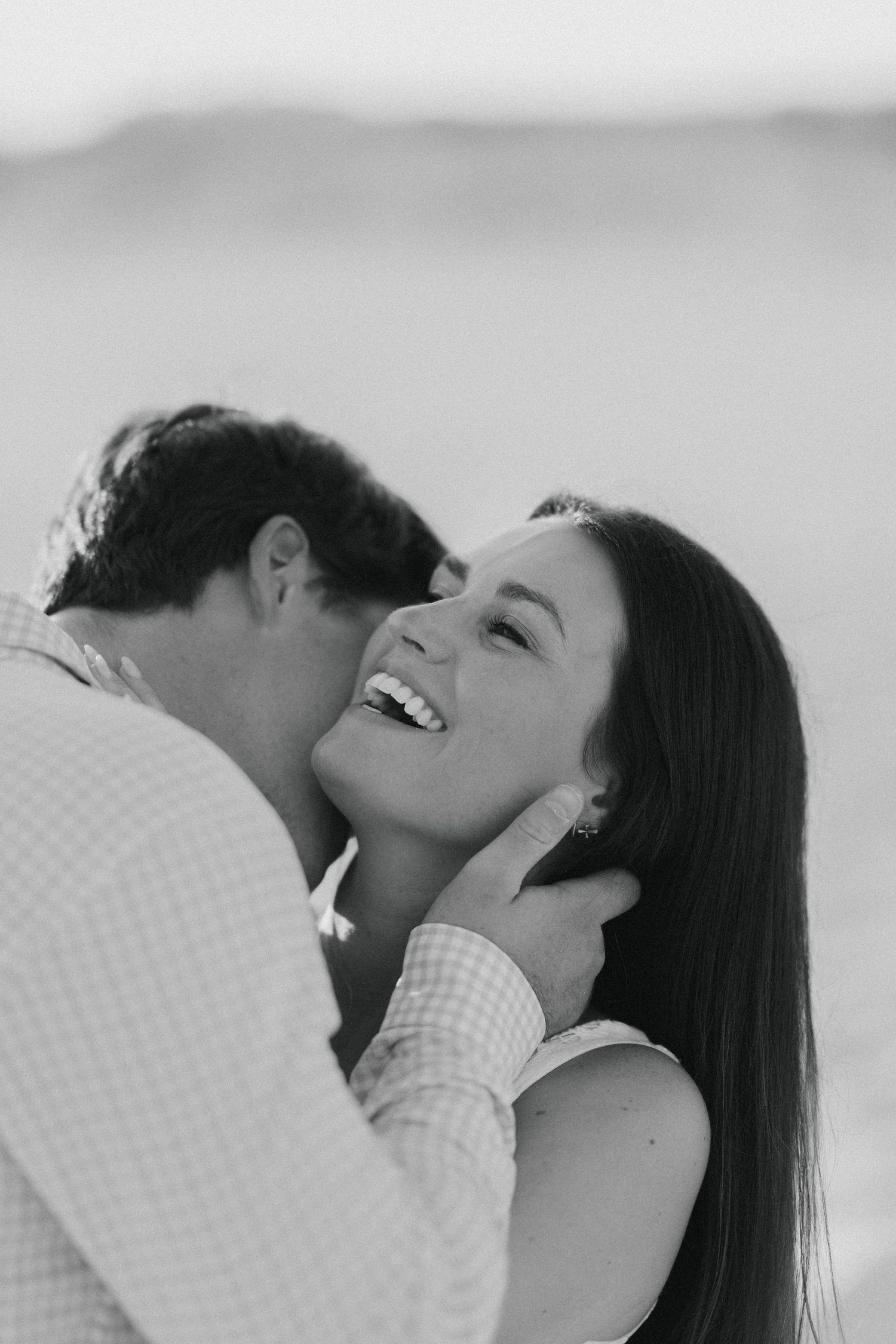 Black and white romantic portrait capturing joy and laughter at the beach.