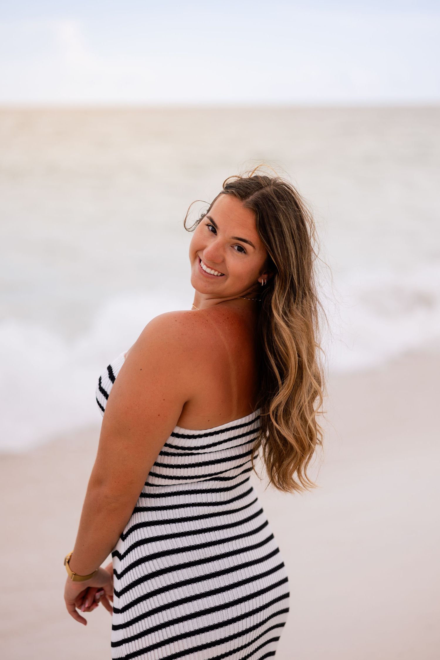 A person in a striped dress poses playfully on the beach in a series of candid shots.