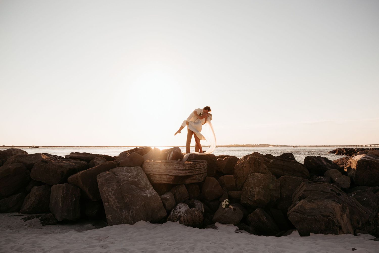 A couple stands among rocky coastal cliffs during sunset creating a romantic silhouette.