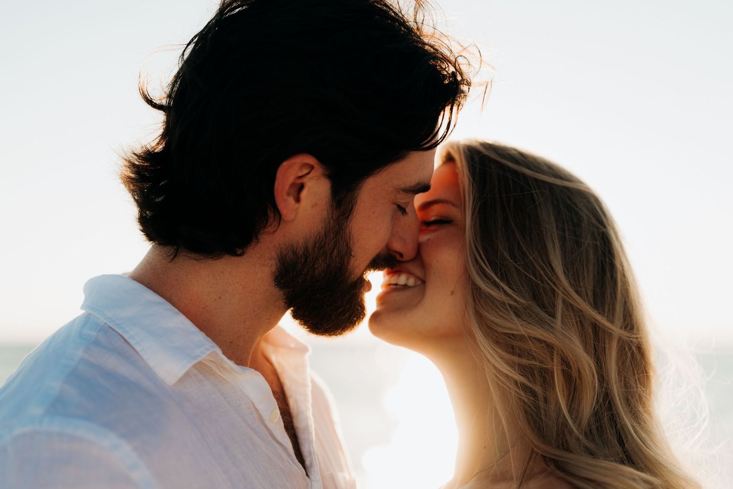 Silhouetted couple sharing a romantic kiss at sunset with warm golden light in the background.