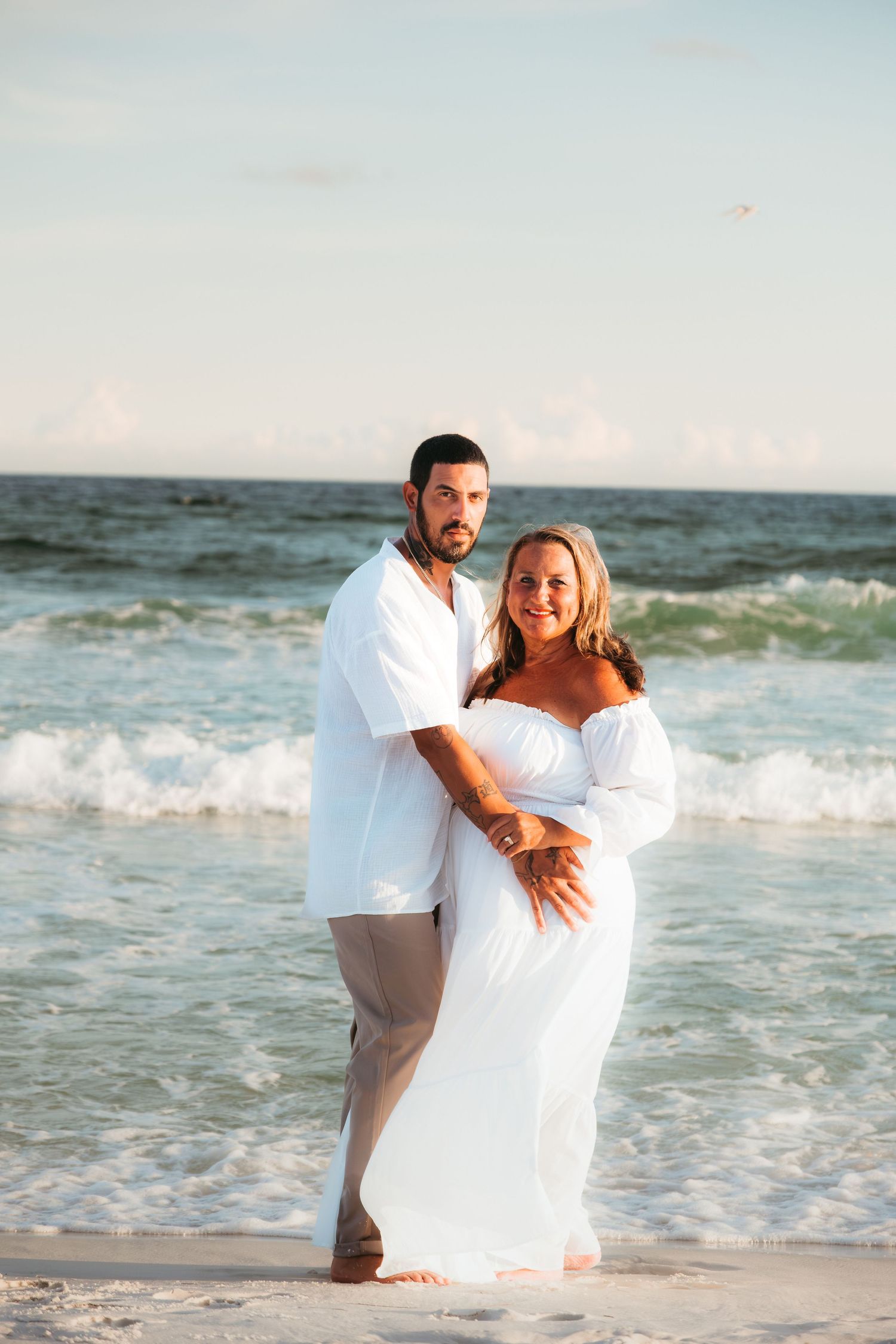 A romantic beach photoshoot with waves crashing in the background at sunset.