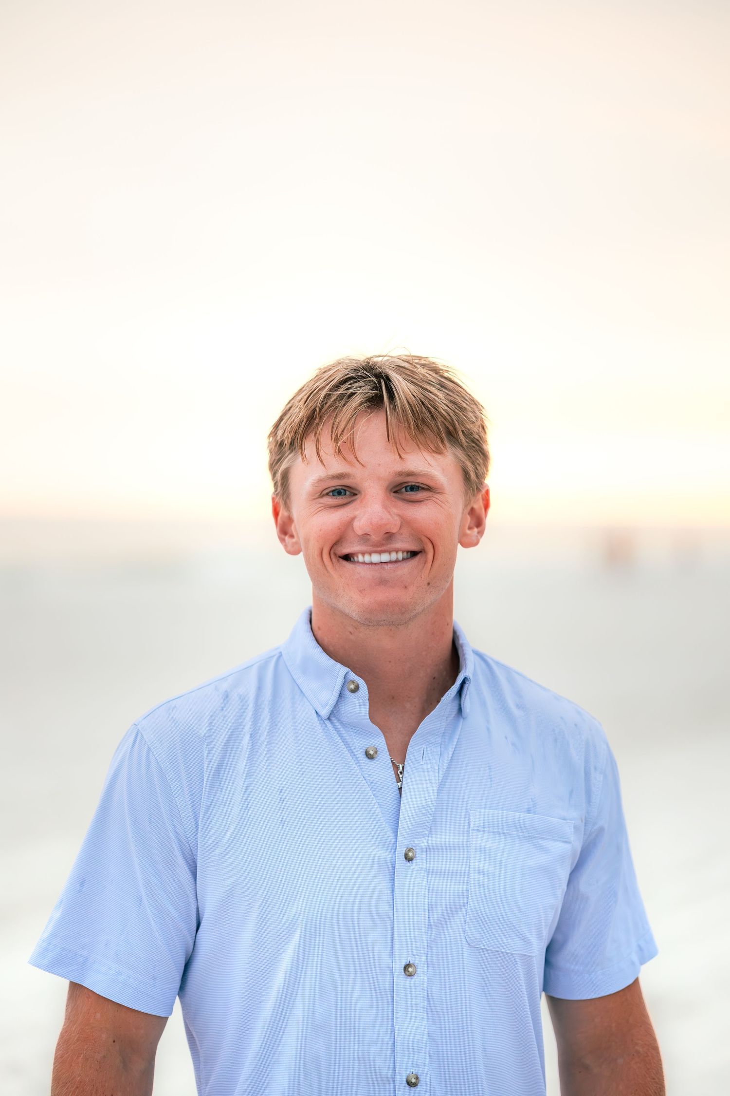 Portrait in light blue button-down shirt with warm sunset lighting.
