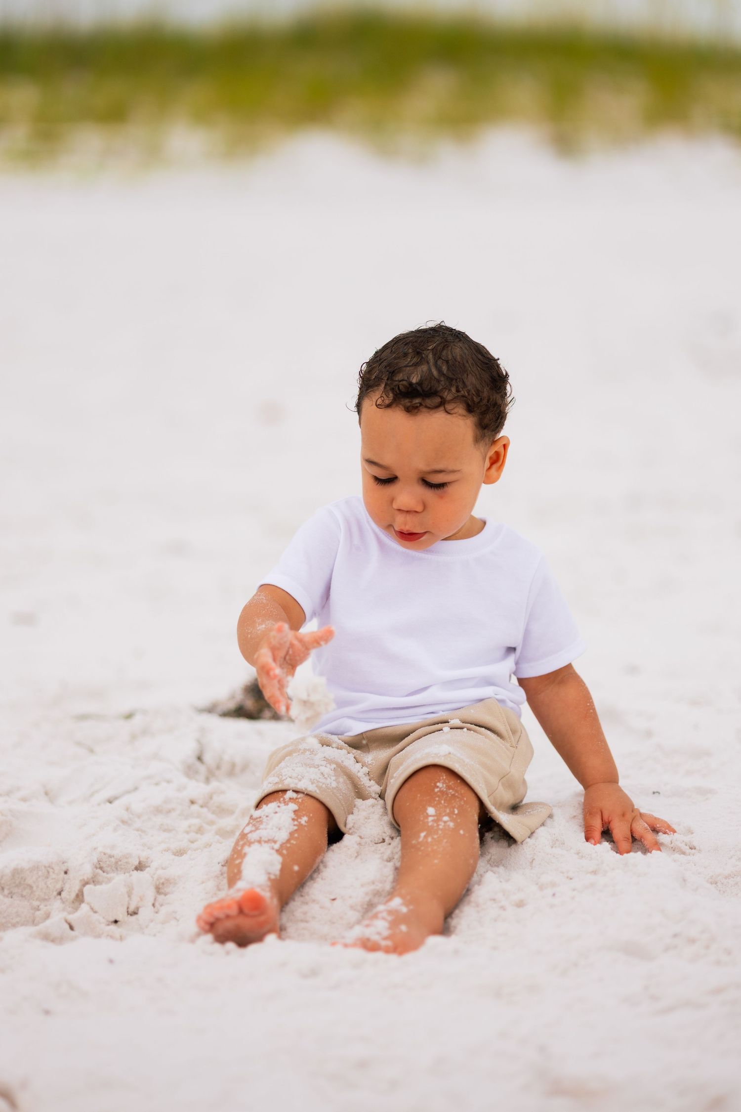 Small child playing in soft white beach sand wearing khaki shorts and white t-shirt.