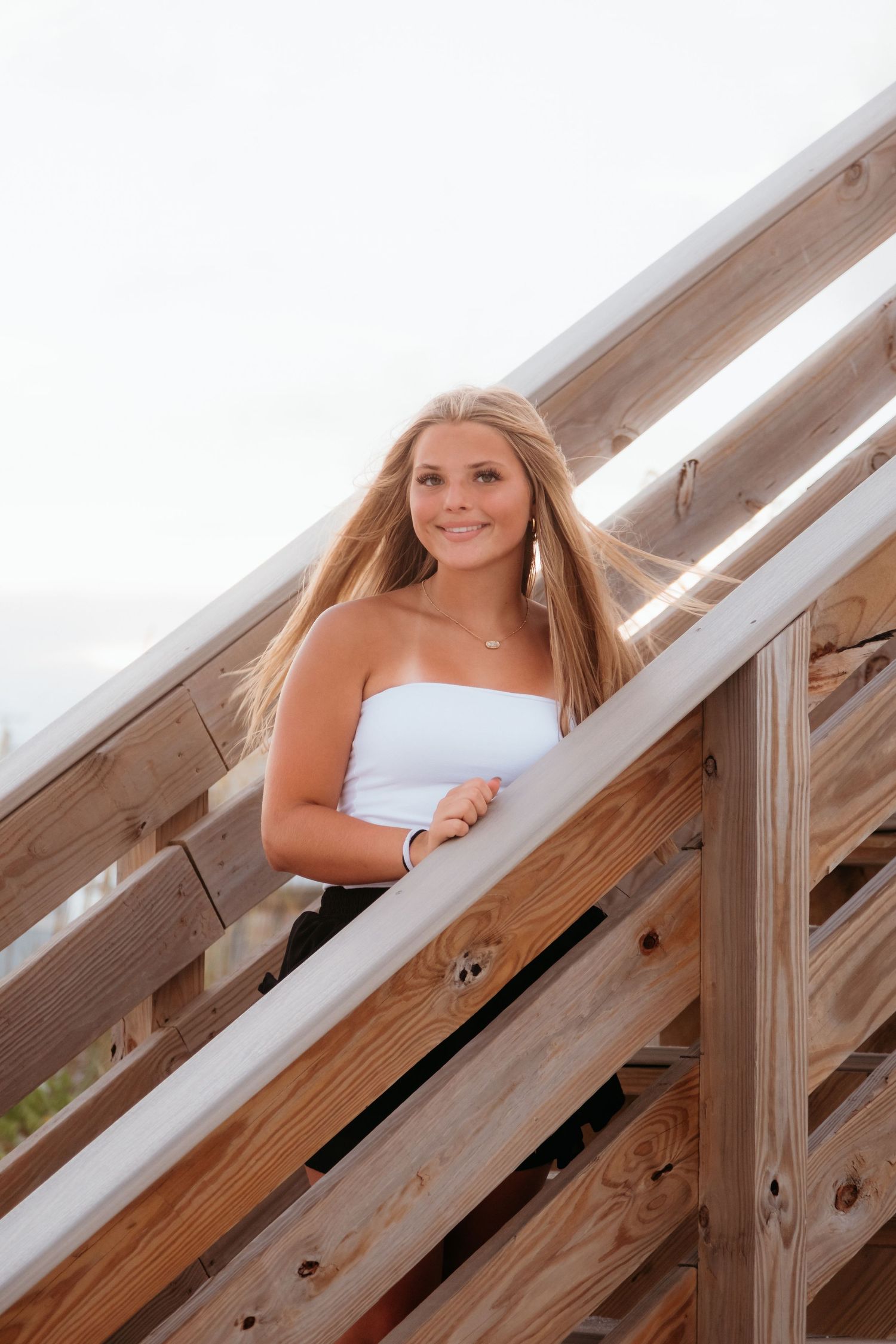 Behind wooden railings on a bright sunny day wearing a white top.