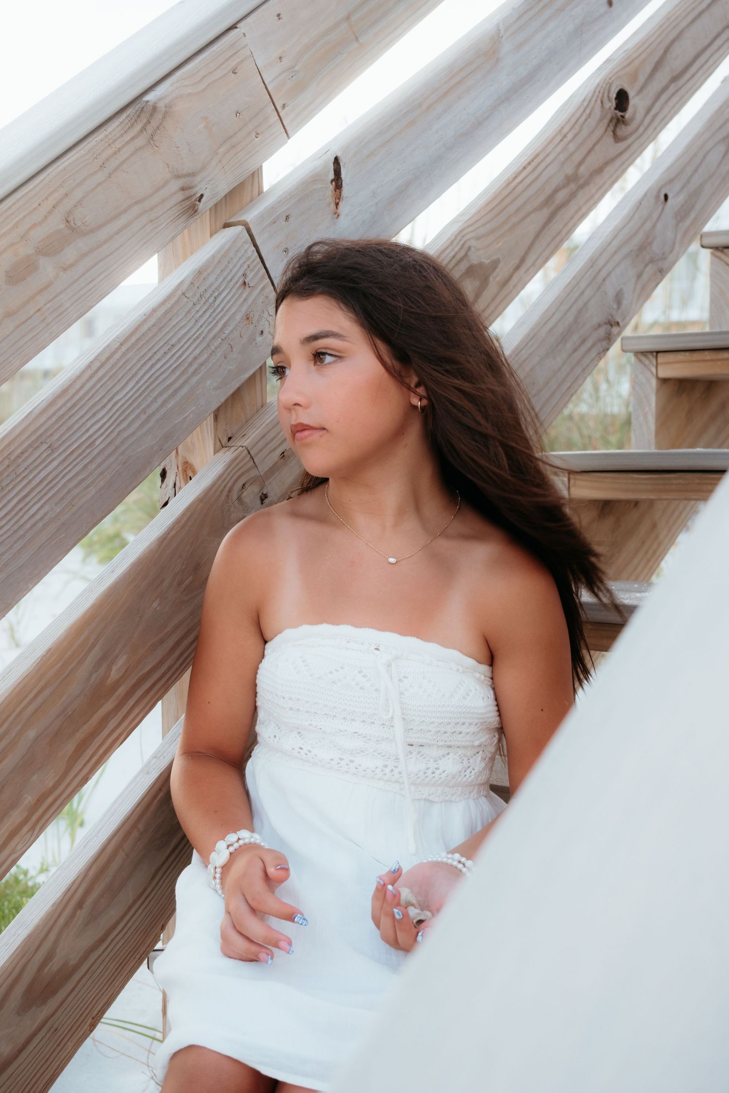 Woman in white dress walking on wooden boardwalk at beach during sunset.