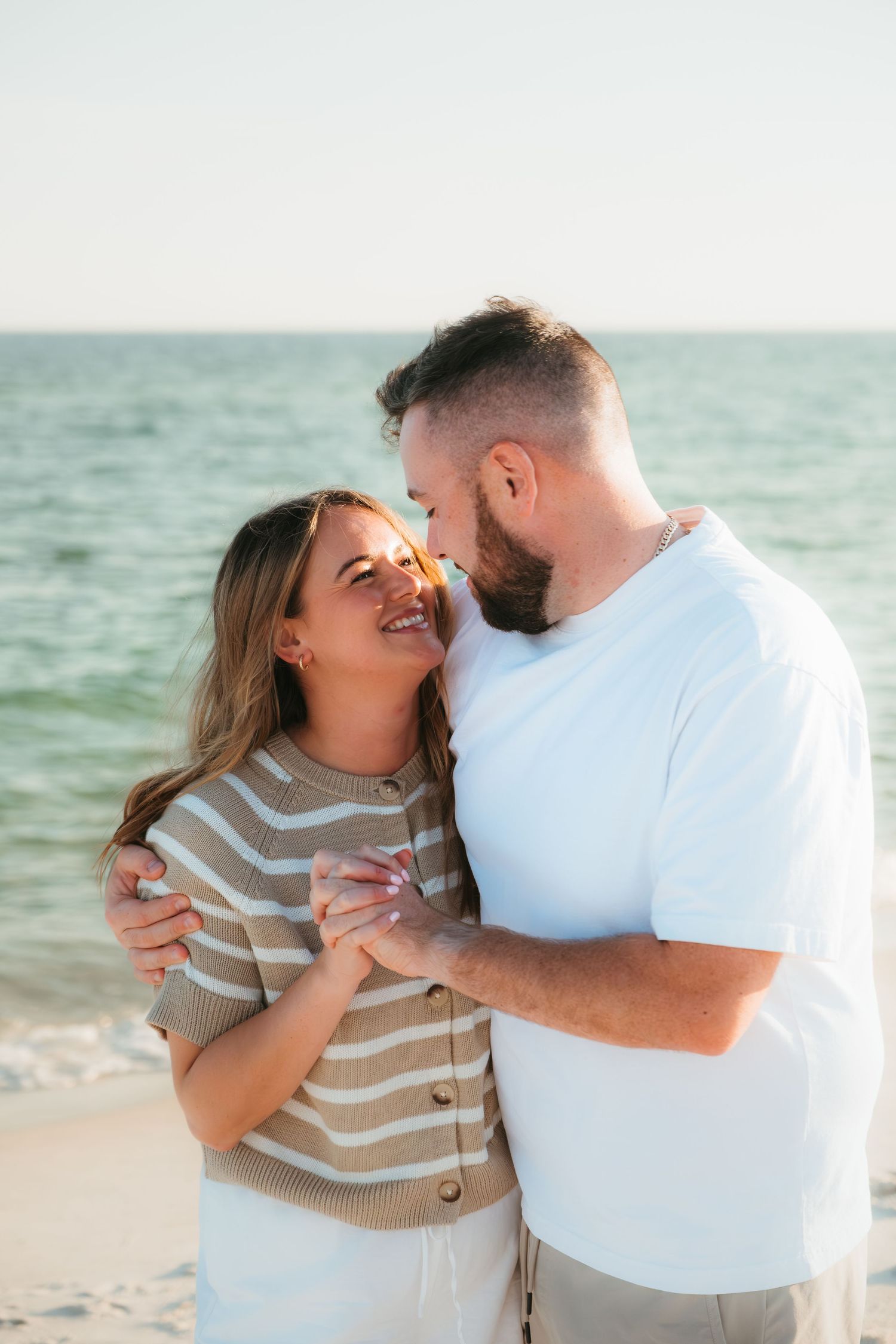 Romantic beach photoshoot with couple in white and striped outfits.