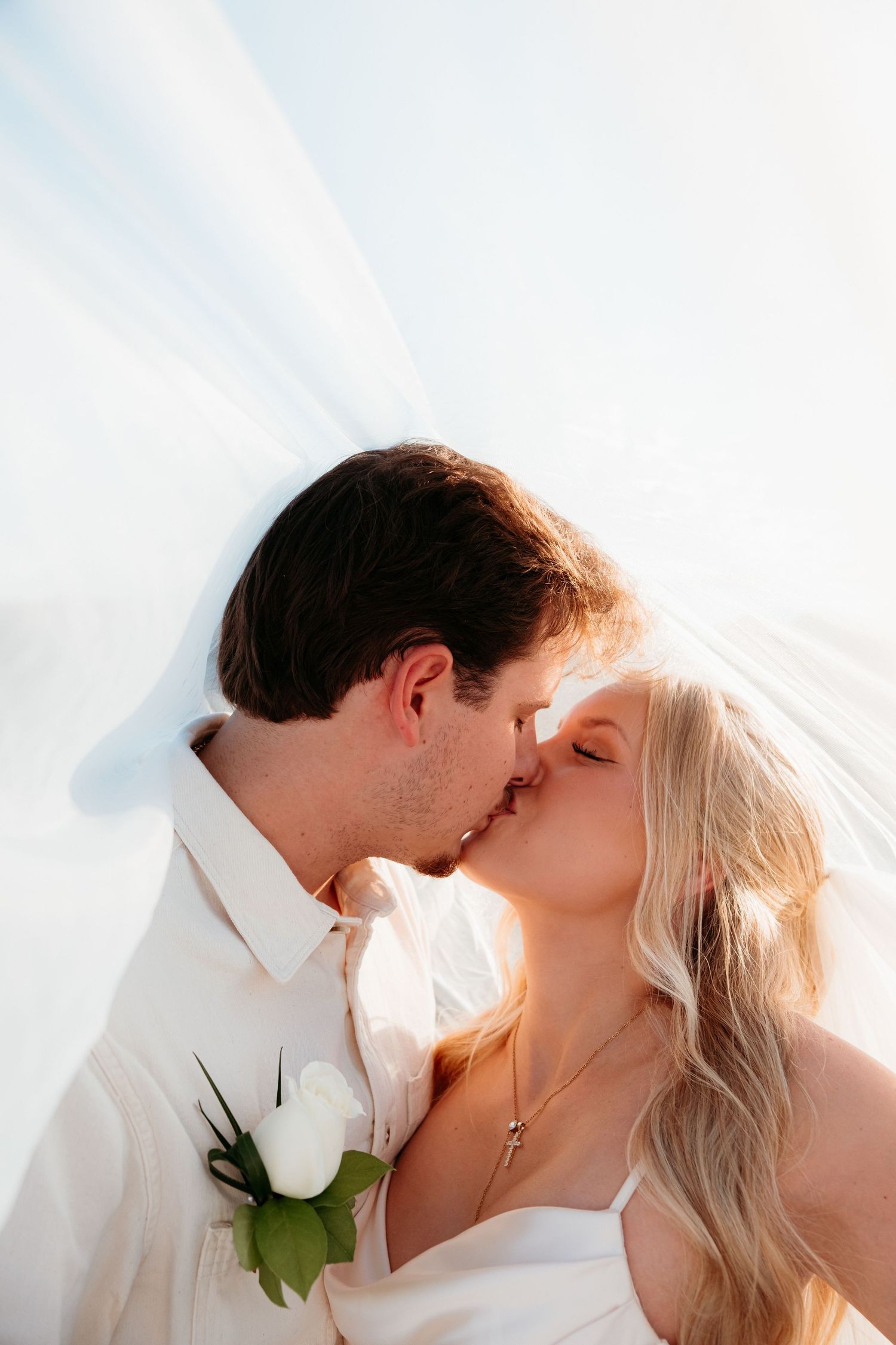 Romantic seaside wedding moment with white rose boutonniere and wedding veil.