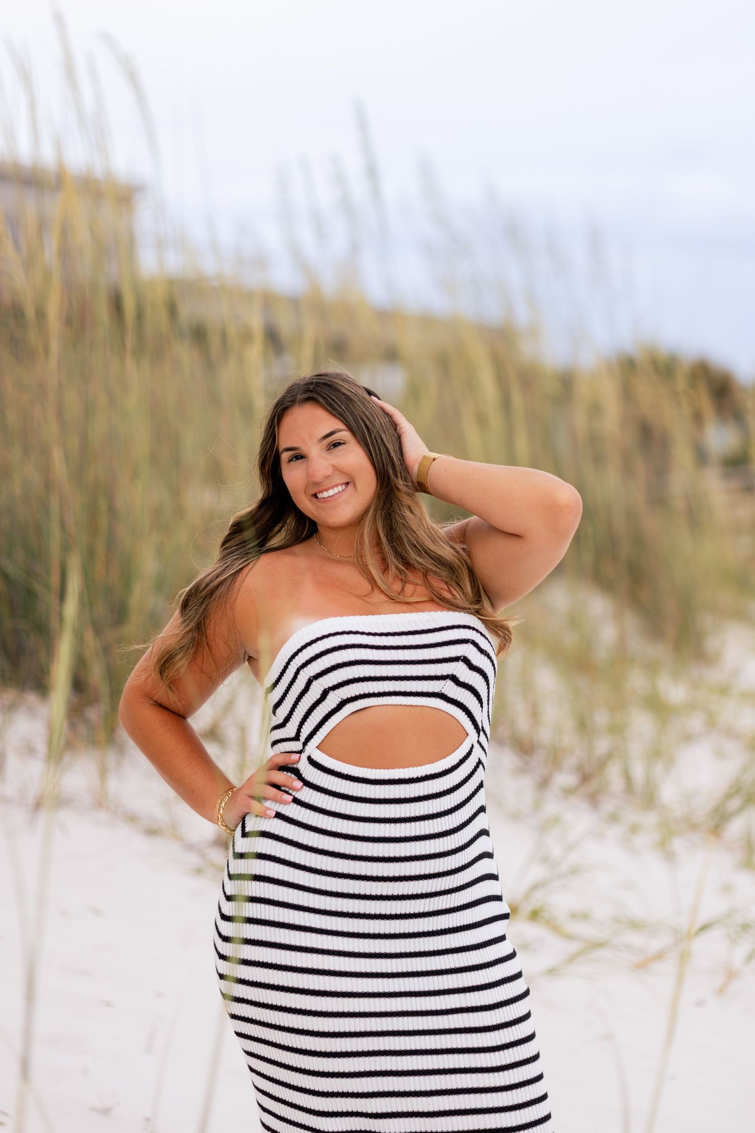 Beach photoshoot featuring a black and white striped dress against white sand dunes.
