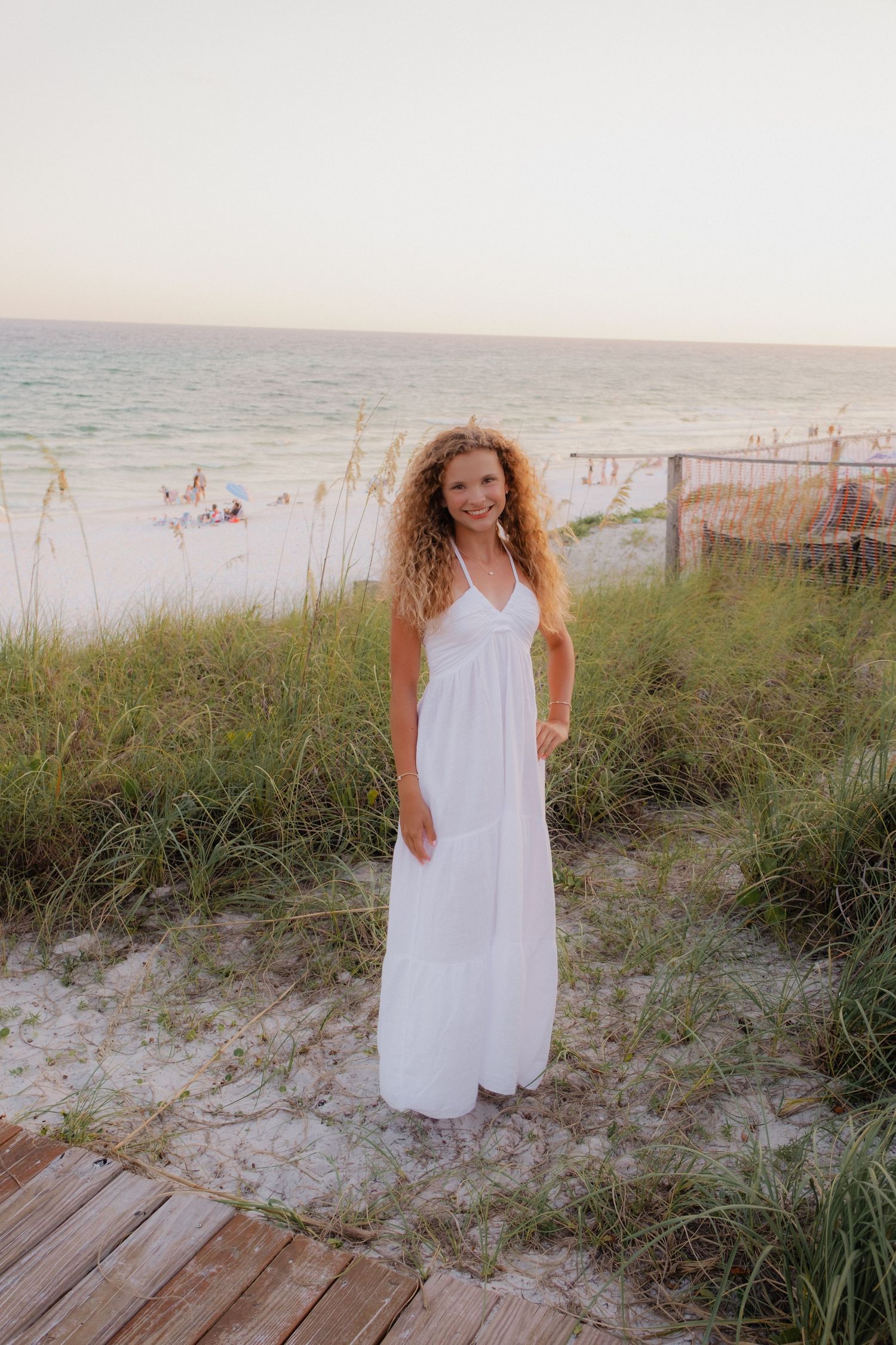 Woman in white sundress posing on beach boardwalk at dusk.